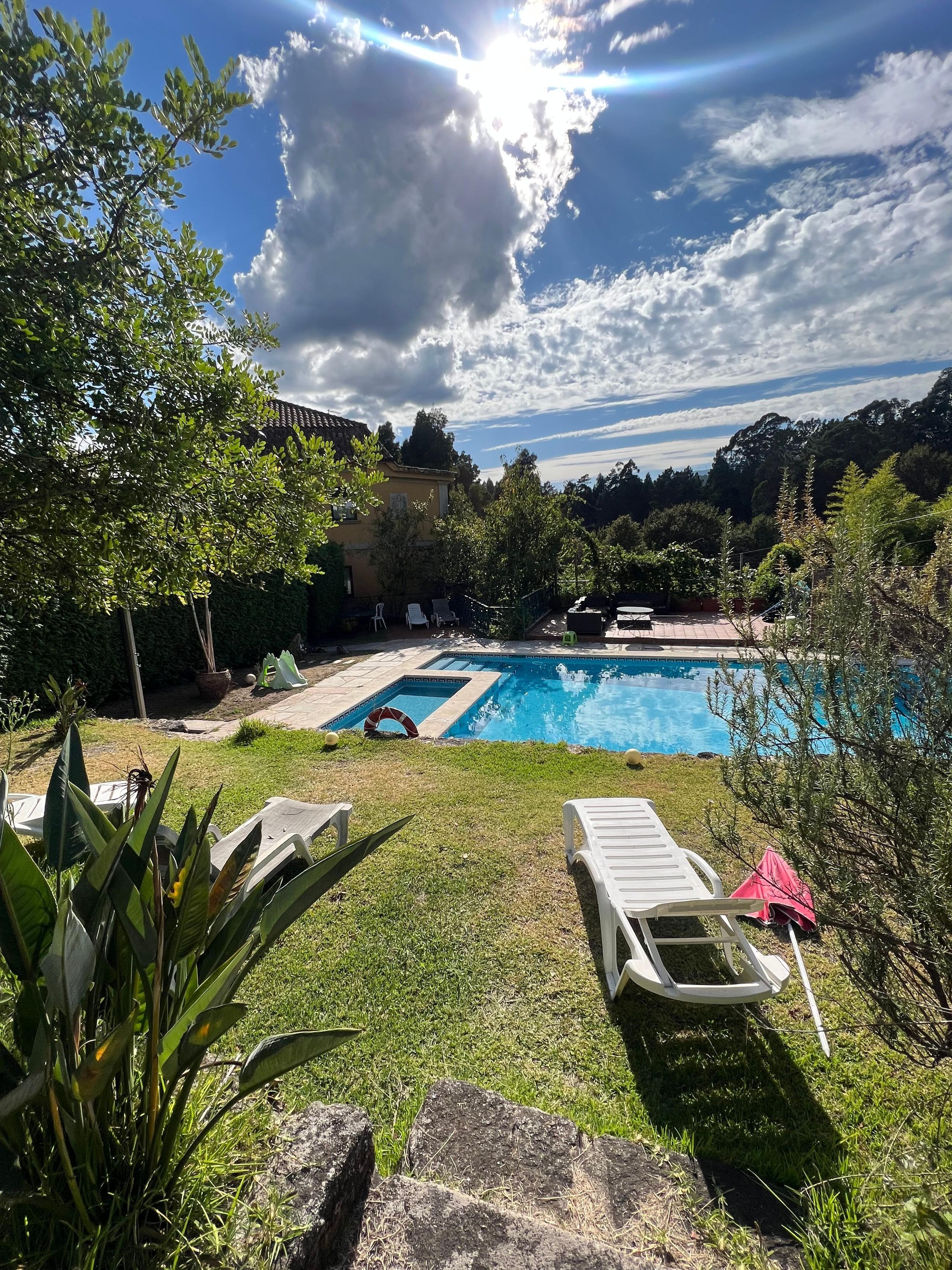 View of the outdoor swimming pool and garden area with sun loungers, surrounded by trees under a dramatic sky