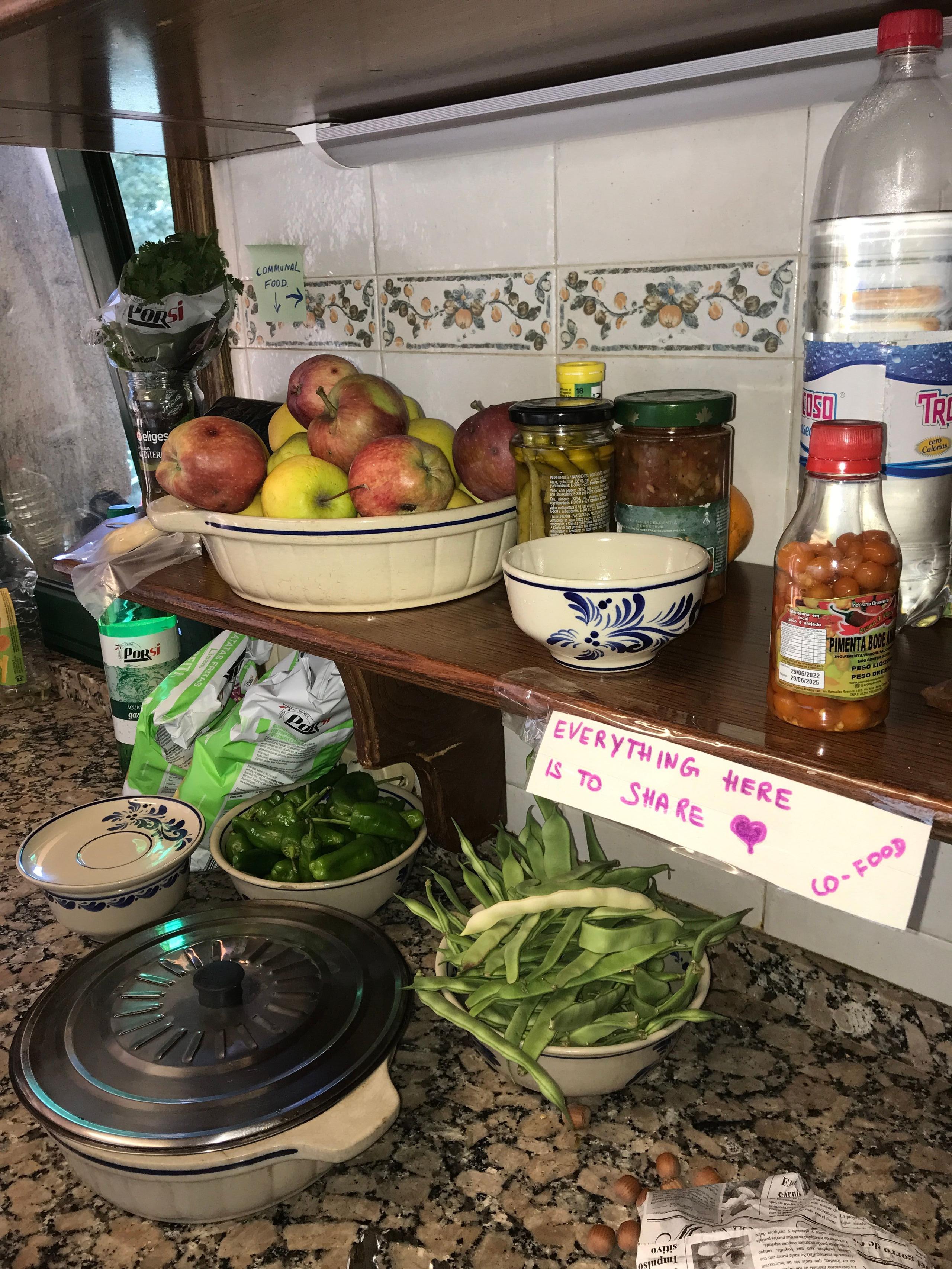 Shared kitchen counter with fresh fruit, vegetables and a sign reading 'Everything here is to share'