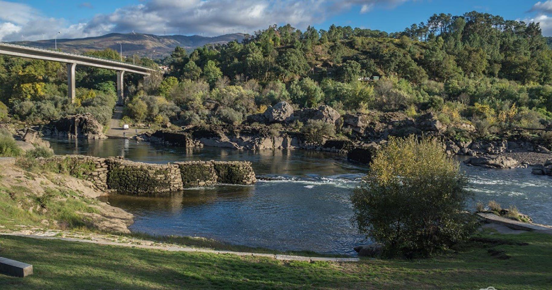 Scenic view of the Miño river with a bridge, rocky banks and green hills in Galicia