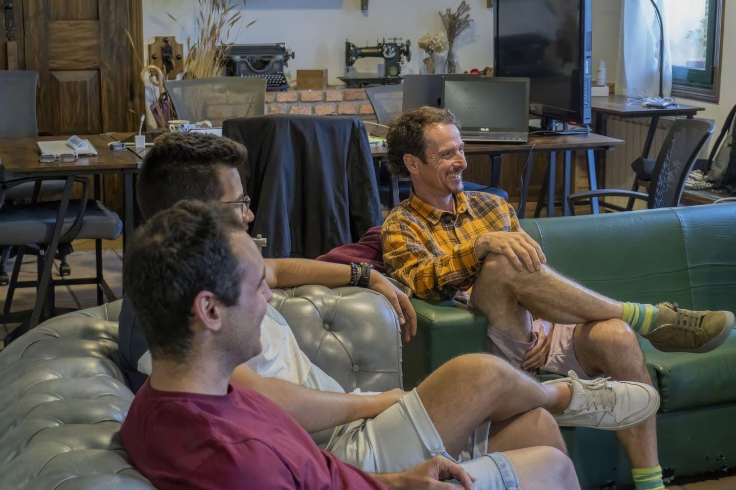 Three guests relaxing and chatting on sofas in the coworking space with desks and vintage decor in the background