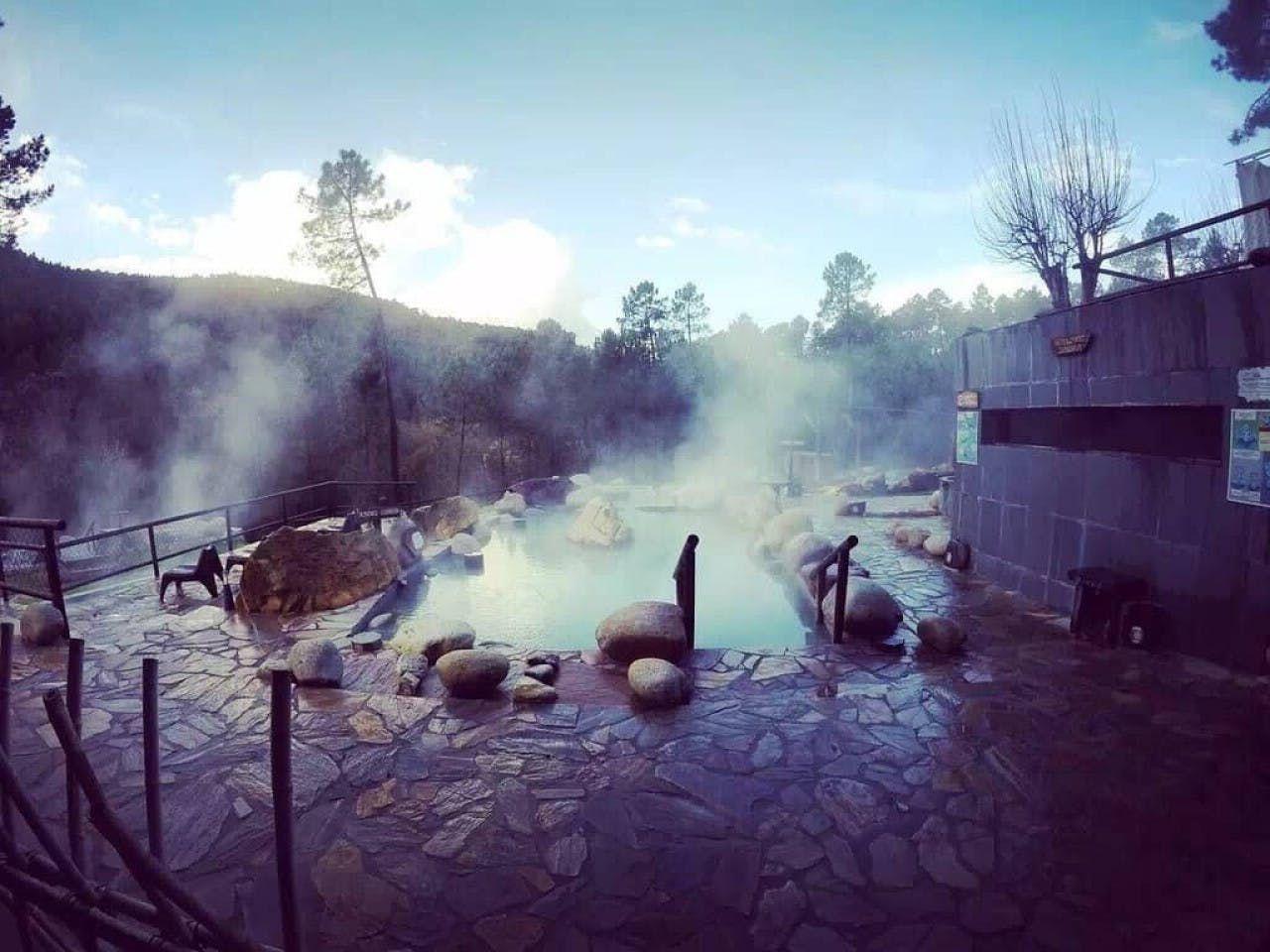 Steaming outdoor hot springs at dusk with rocks and pine trees in the background