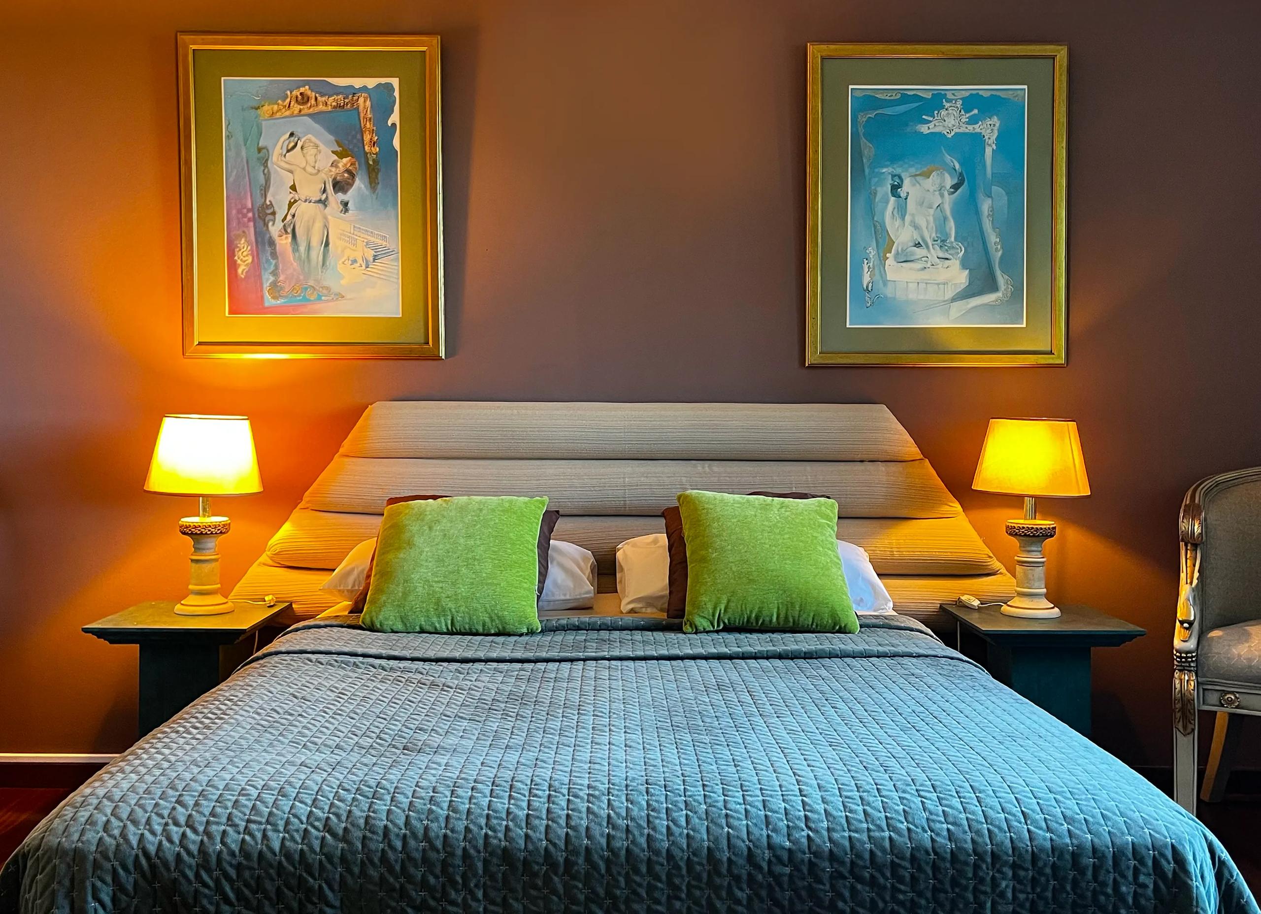 Close-up of the double bed with warm lighting and framed artwork in Room 07 Girassol