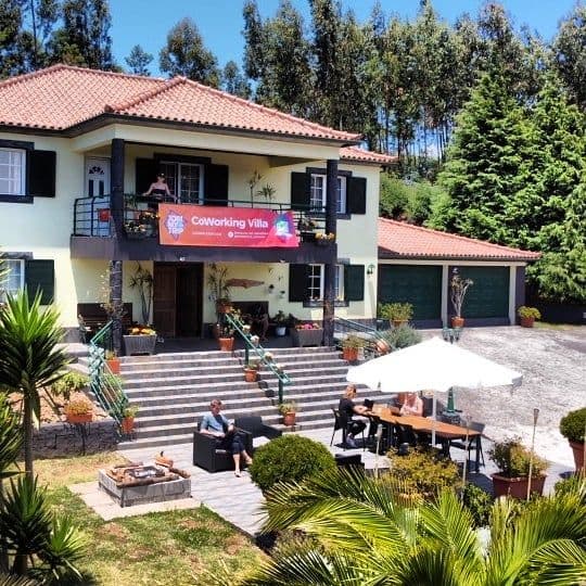 Exterior view of the Homeoffice Madeira CoWorking Villa with a banner, guests on the terrace and balcony