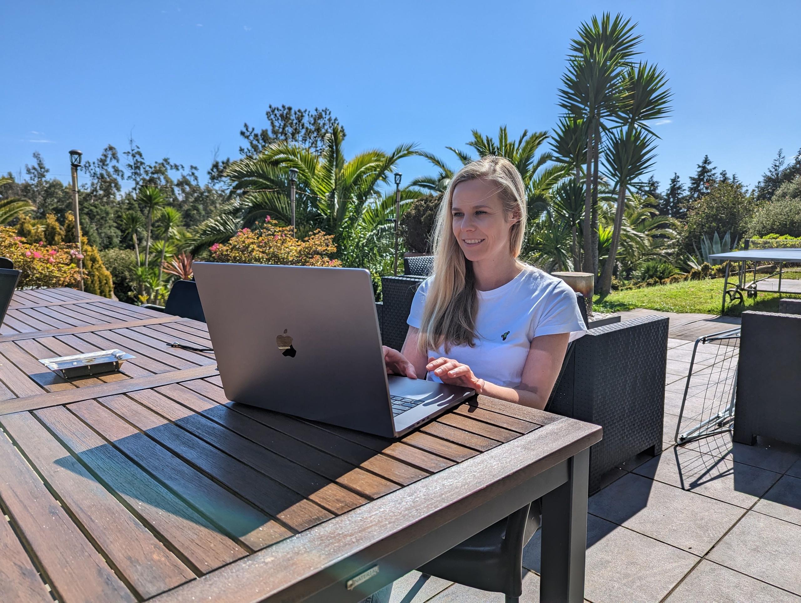 Lina working on her laptop amidst the lush garden of Homeoffice Madeira, surrounded by palm trees and a breathtaking sea view