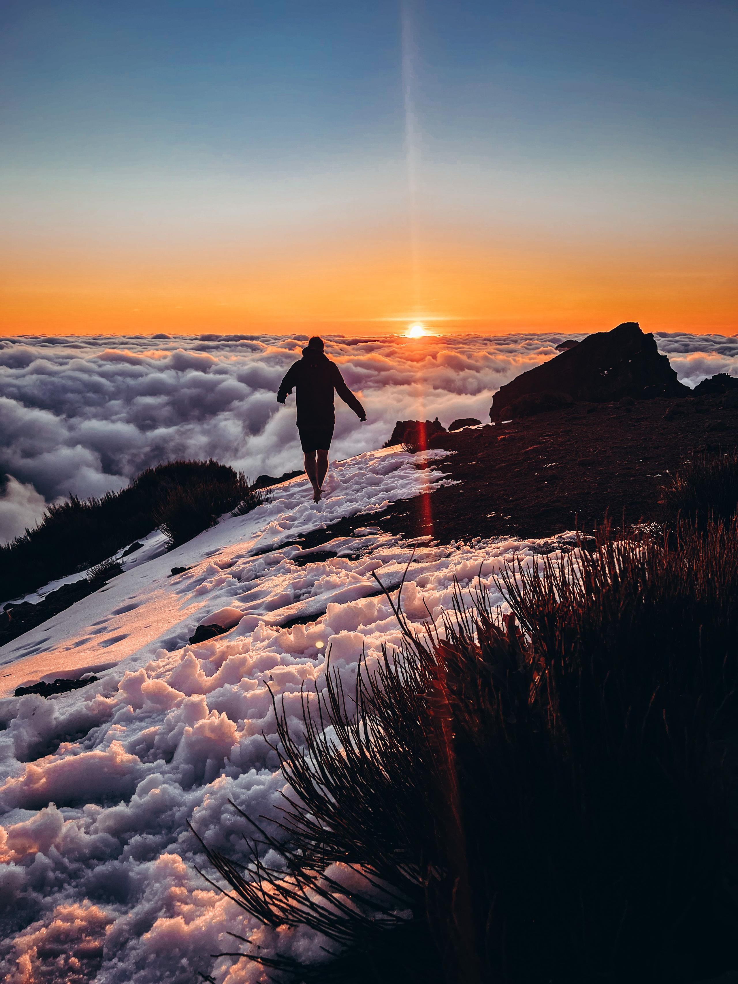 Silhouette of a hiker walking on a snowy mountain ridge above the clouds at sunset on Madeira