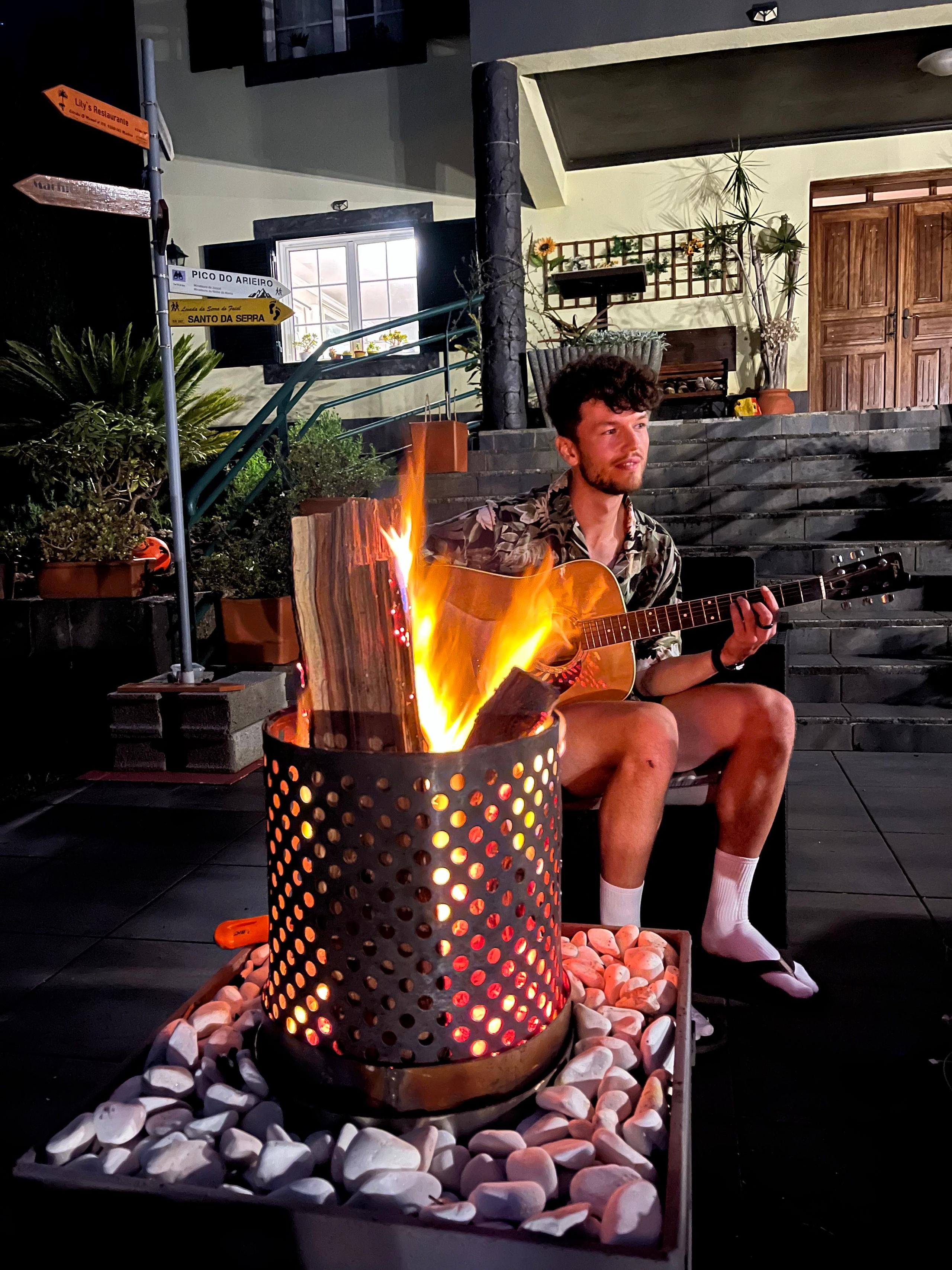 ulius, a guest at Homeoffice Madeira, entertains his fellow guests with soulful guitar melodies during a bonfire gathering, bringing everyone together with the power of music.