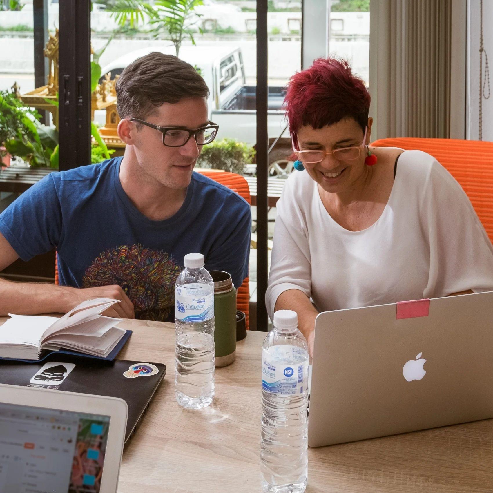 Two people working together on a laptop at a coworking desk