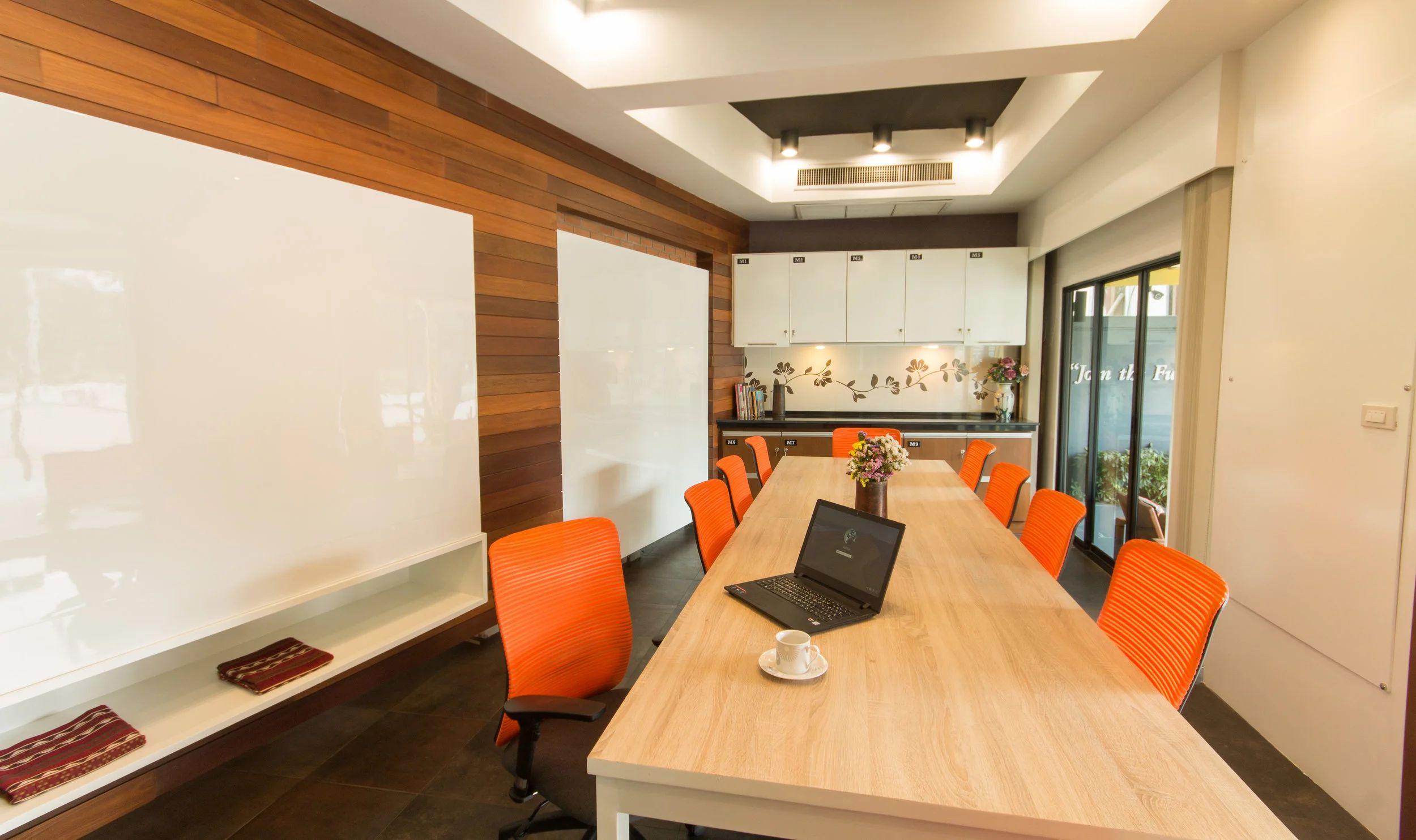 Conference room with long table, orange ergonomic chairs, whiteboard and projector screen viewed from the side