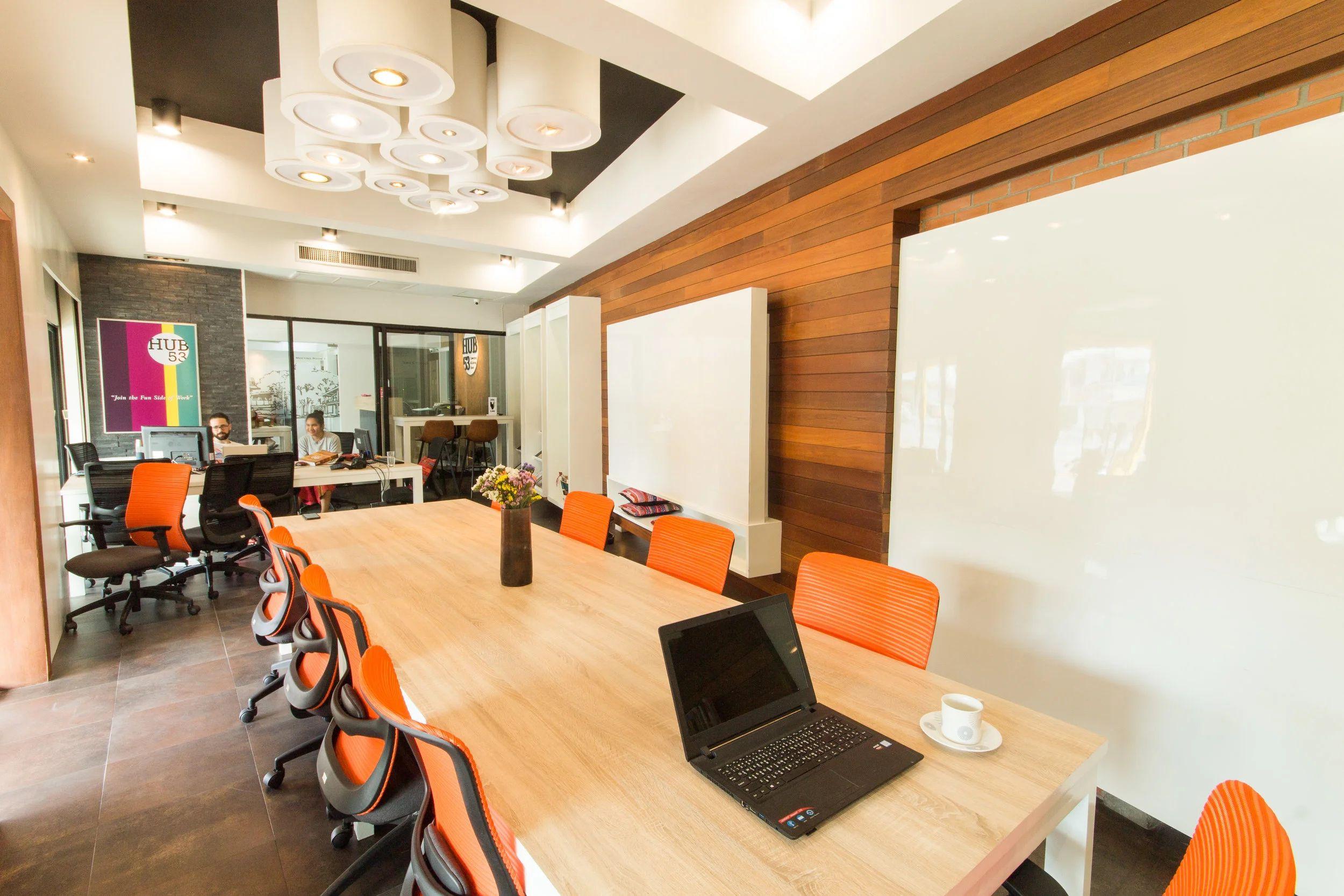 Conference room with long table, orange ergonomic chairs, whiteboard and projector screen