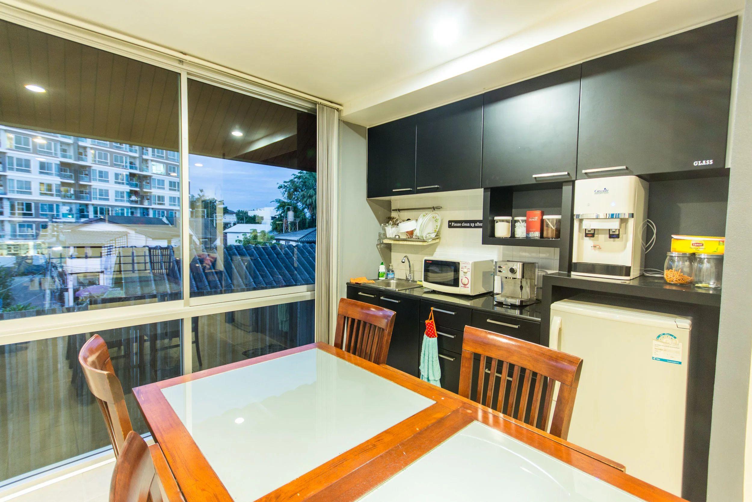 Shared kitchen with dining table, dark cabinets, microwave, coffee machine and large window overlooking the city