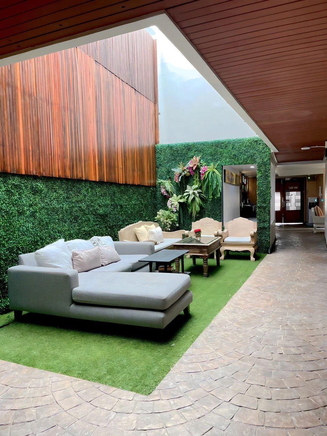 Covered outdoor courtyard with grey sectional sofa, coffee table, green wall and wooden ceiling