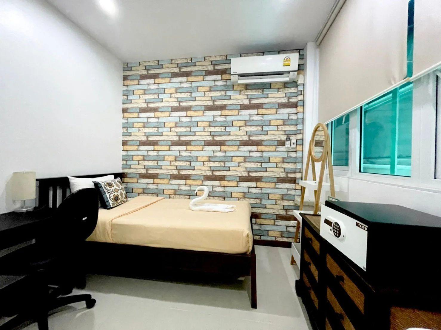 Standard A room with twin bed, brick-pattern accent wall, desk, chair and air conditioning