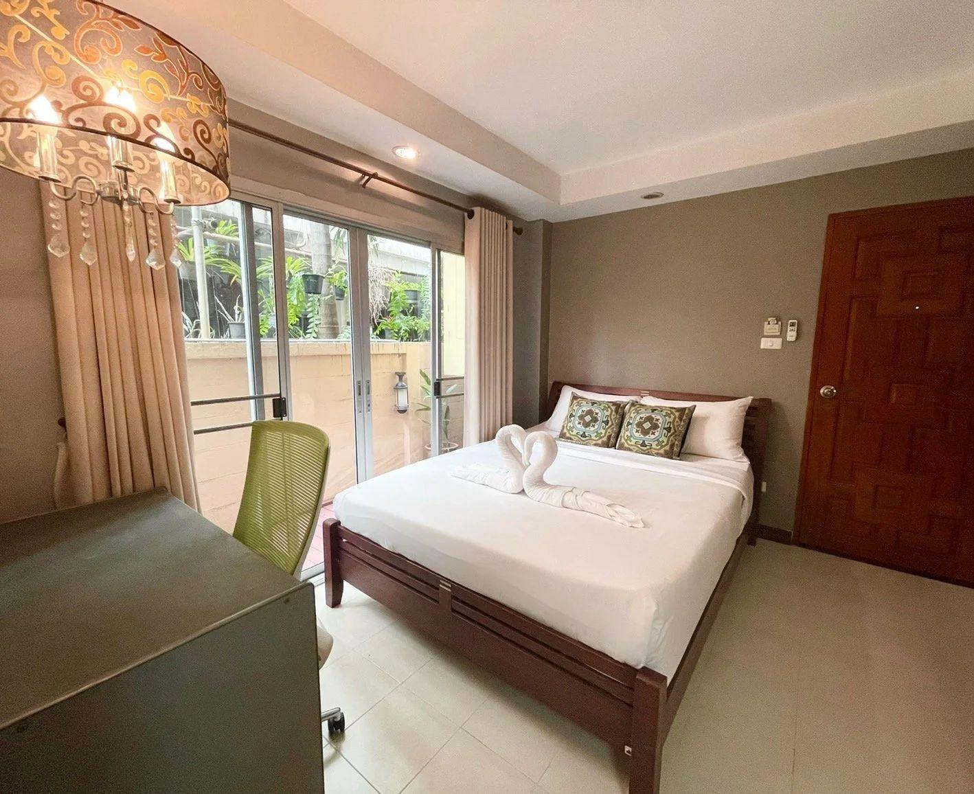 Deluxe room with queen bed, large sliding glass doors opening to a balcony with garden view, desk and decorative lamp