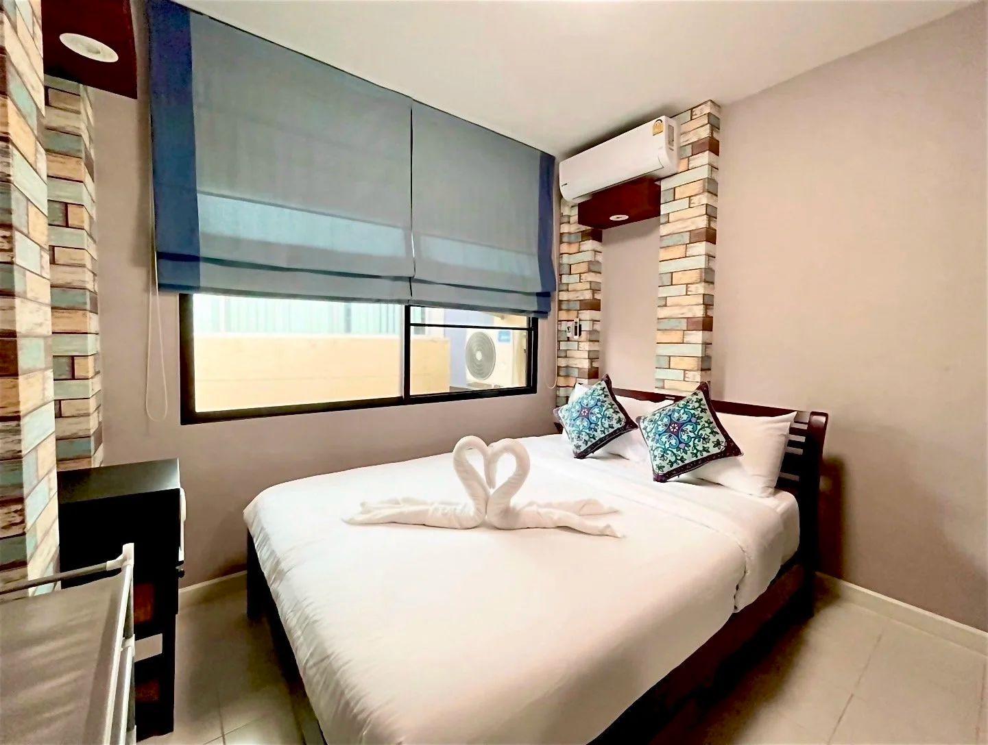 Standard B room with queen bed, blue roller blind, brick-pattern accent wall and air conditioning