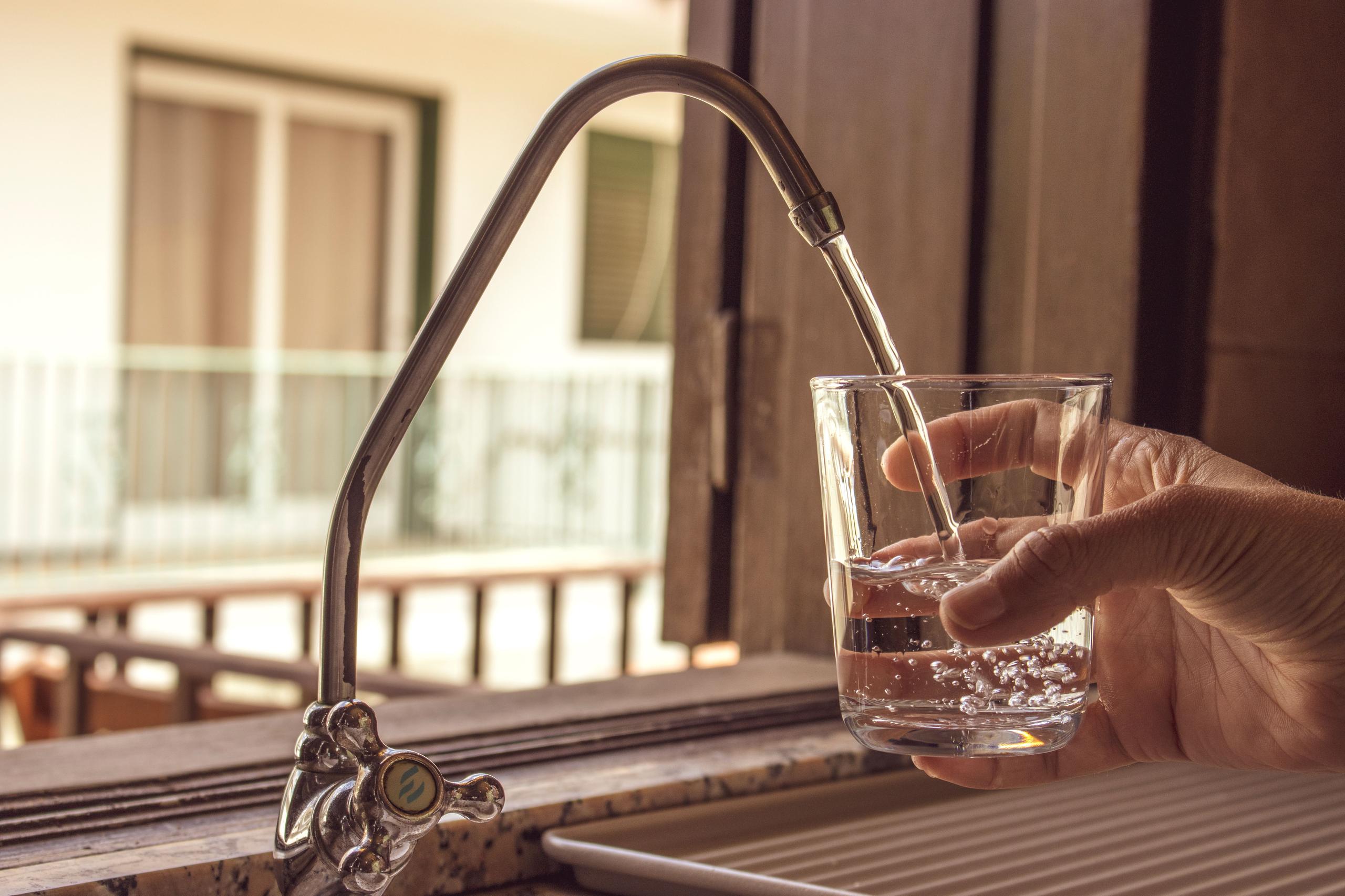 Hand filling a glass of water from a kitchen tap with a view of the balcony in the background