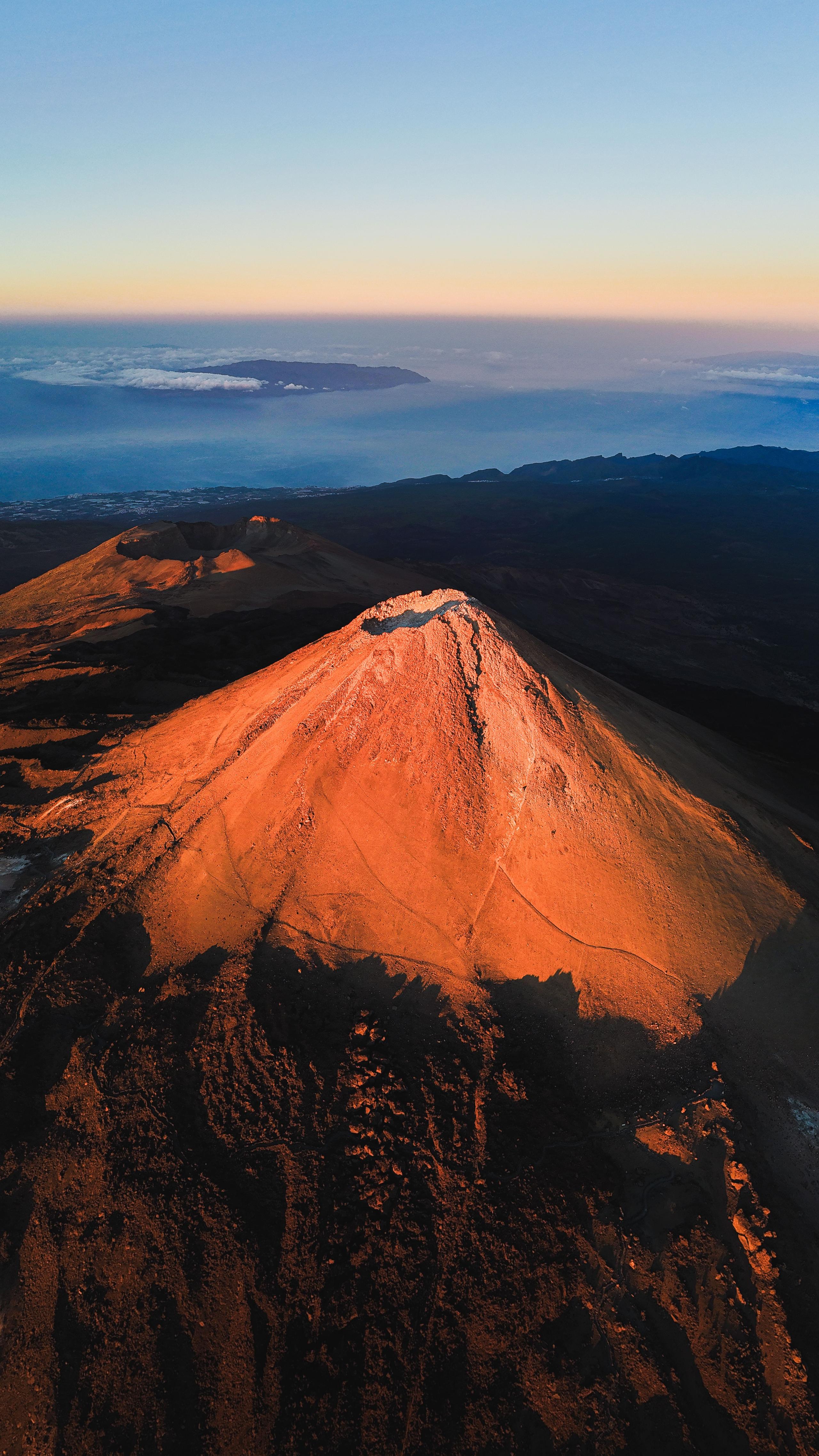 Aerial drone view of the Teide volcano summit glowing orange at sunrise with ocean and clouds in the background