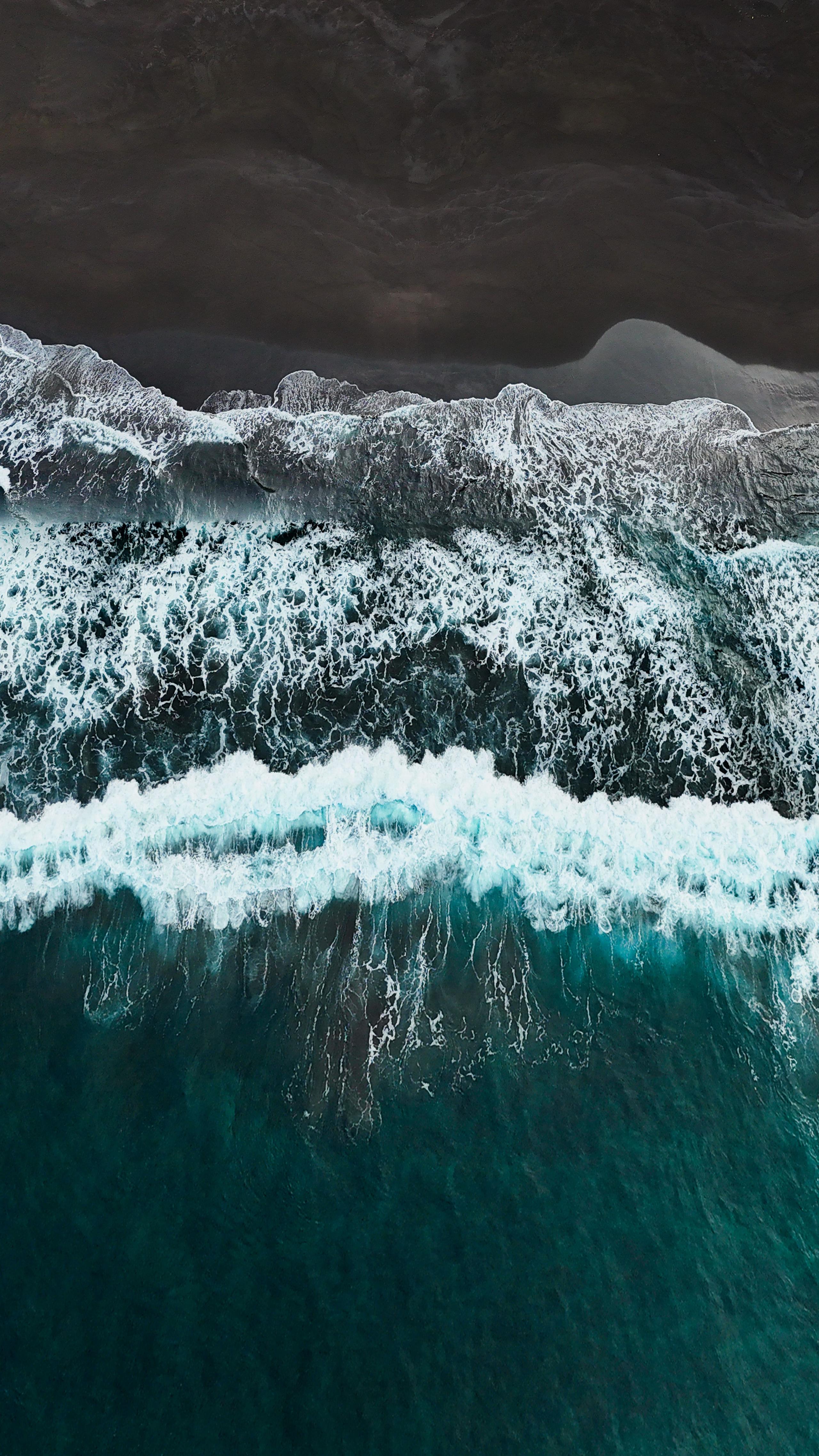 Aerial view of a black sand beach with turquoise ocean waves