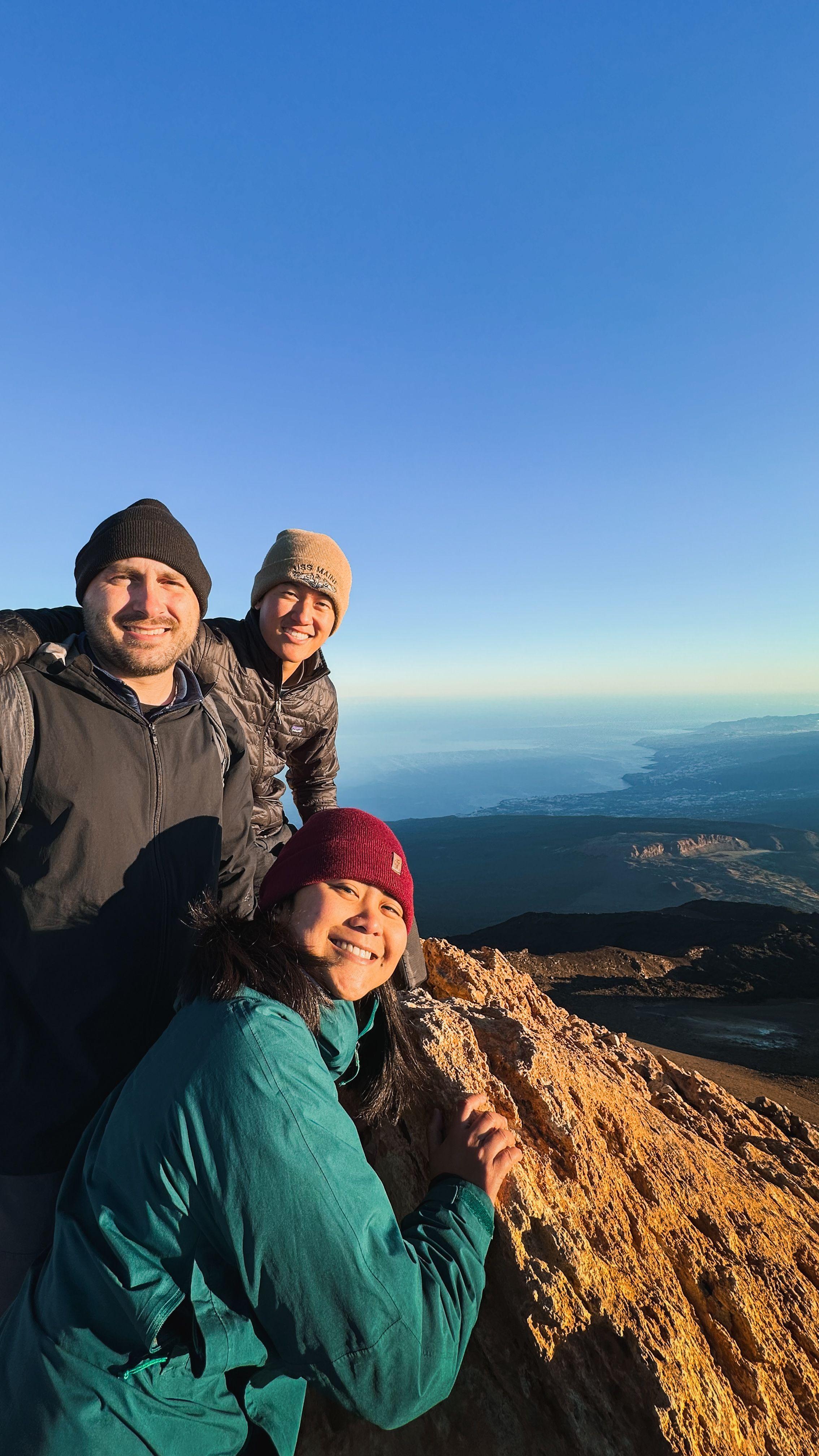 Three community members posing at the summit of Teide volcano with ocean views in the background