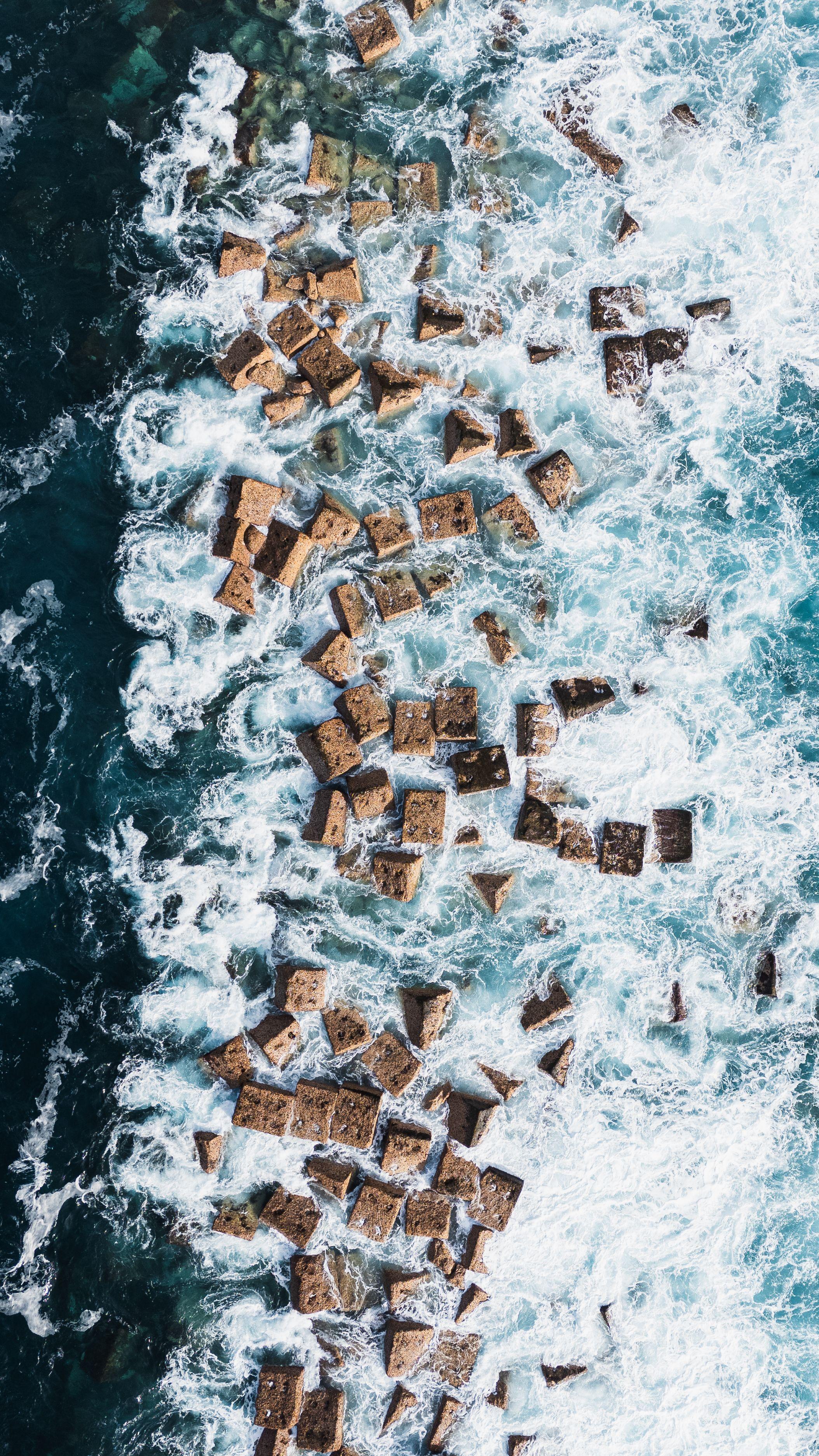 Aerial view of volcanic rock pools with ocean waves crashing around them