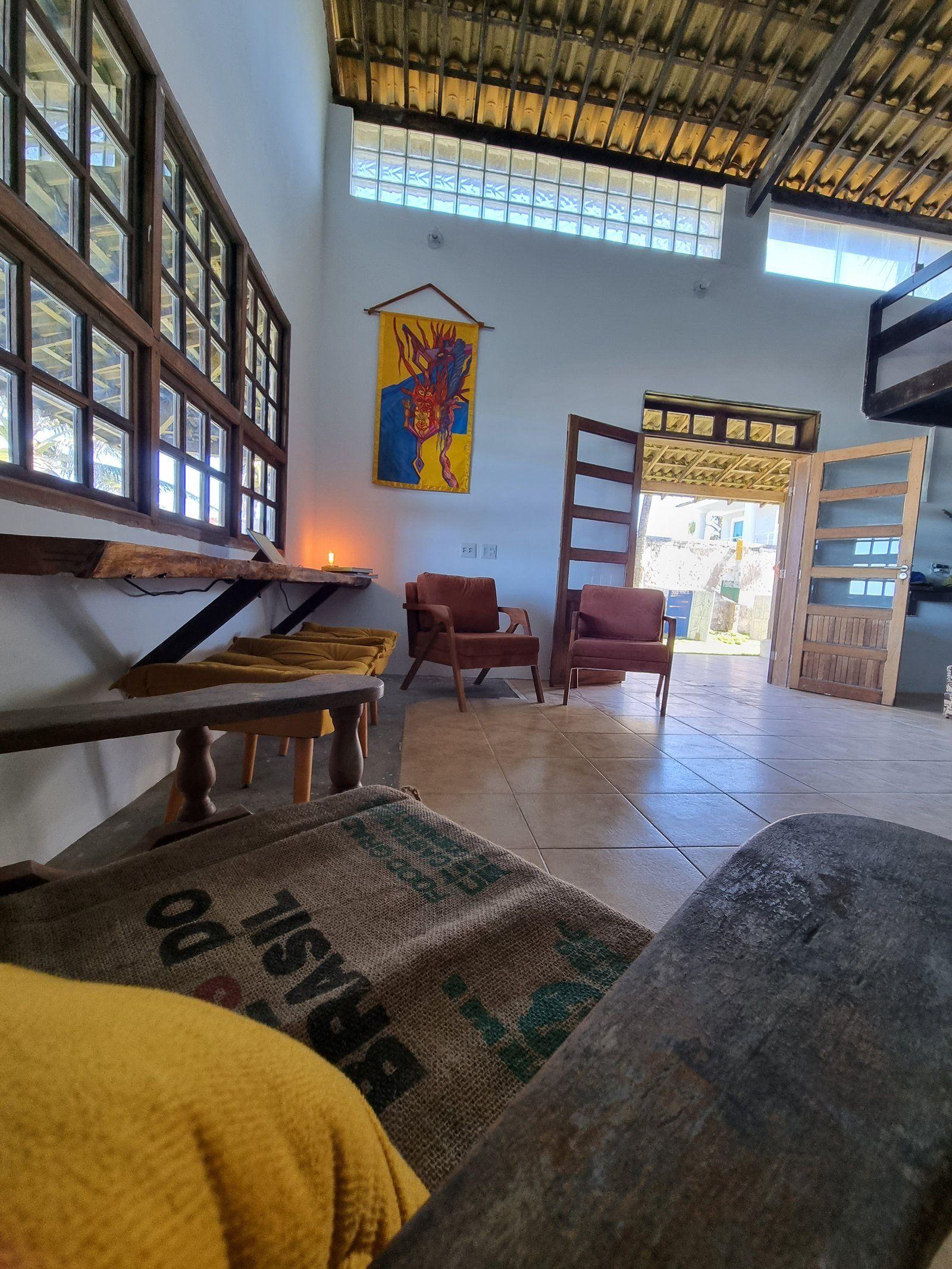 Communal living lounge with a long wooden bench, armchairs, decorative artwork hanging on the wall, and open door.