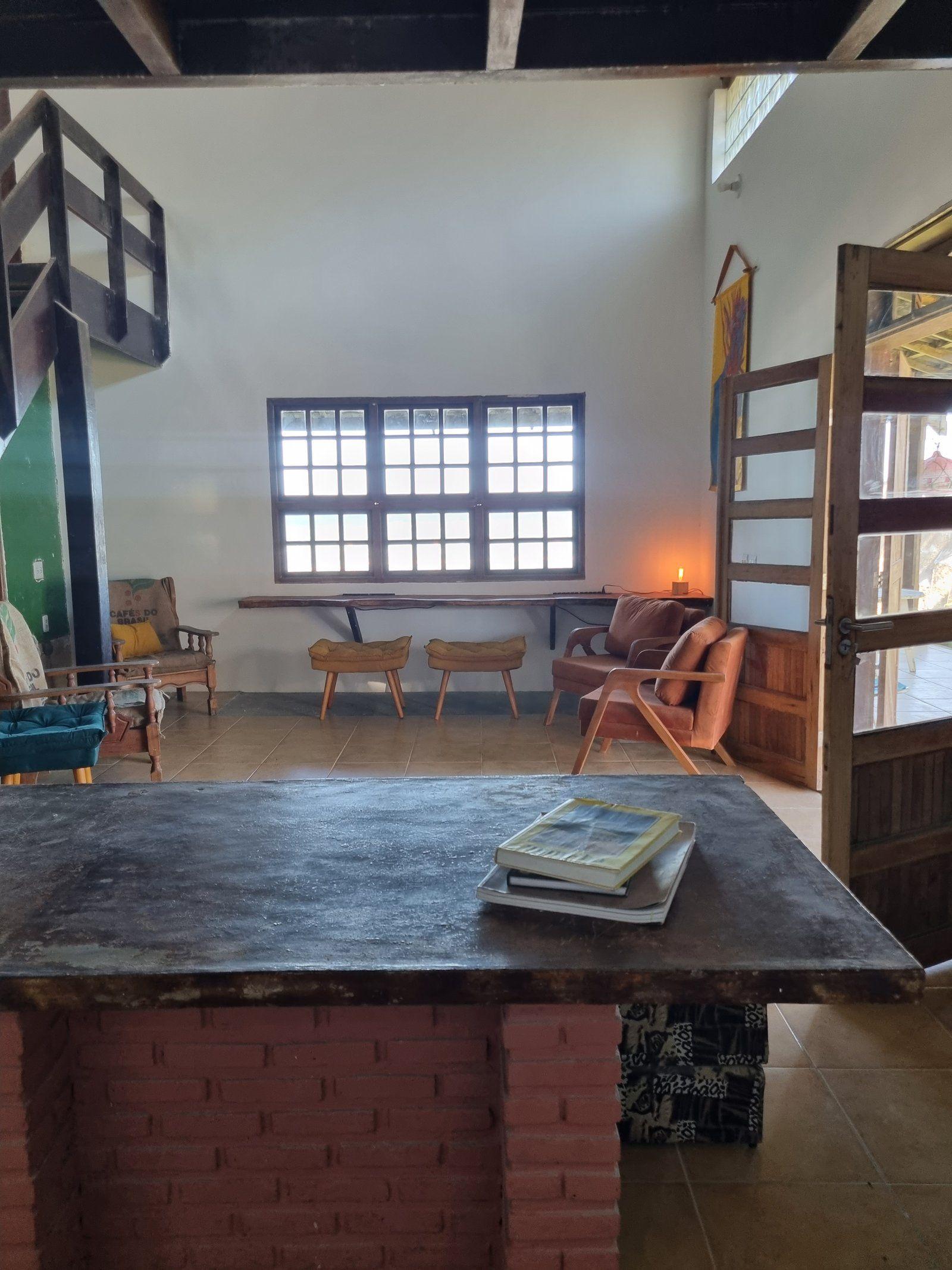 Interior view of the communal living lounge with a long wooden table, armchairs, staircase, and open door to the garden.