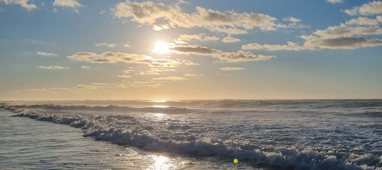 Panoramic view of the beach at sunrise with waves and a golden sky.