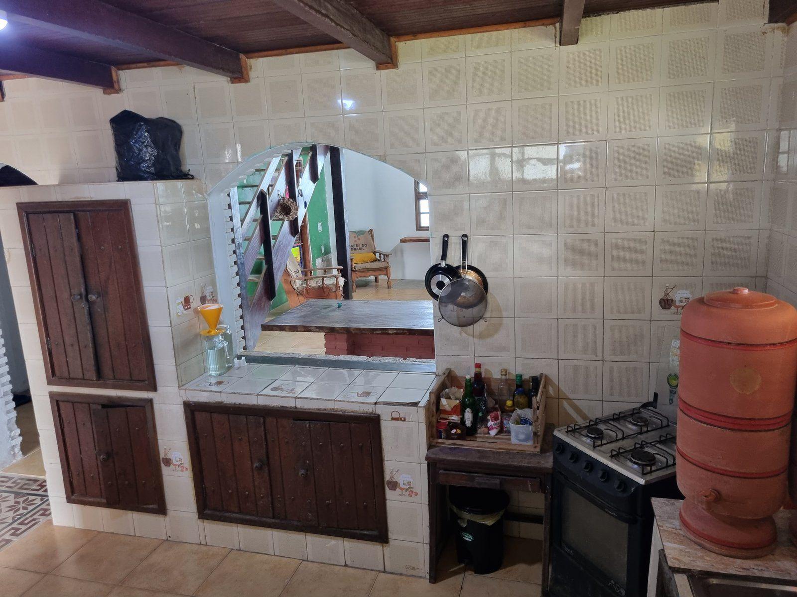 Shared kitchen with tiled walls, wooden cabinets, a gas stove, hanging pans, and a clay water pot.