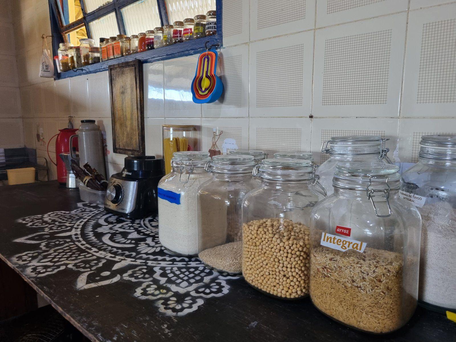 Shared kitchen counter with glass jars of grains and dry goods, a blender, and spice shelves on the wall.