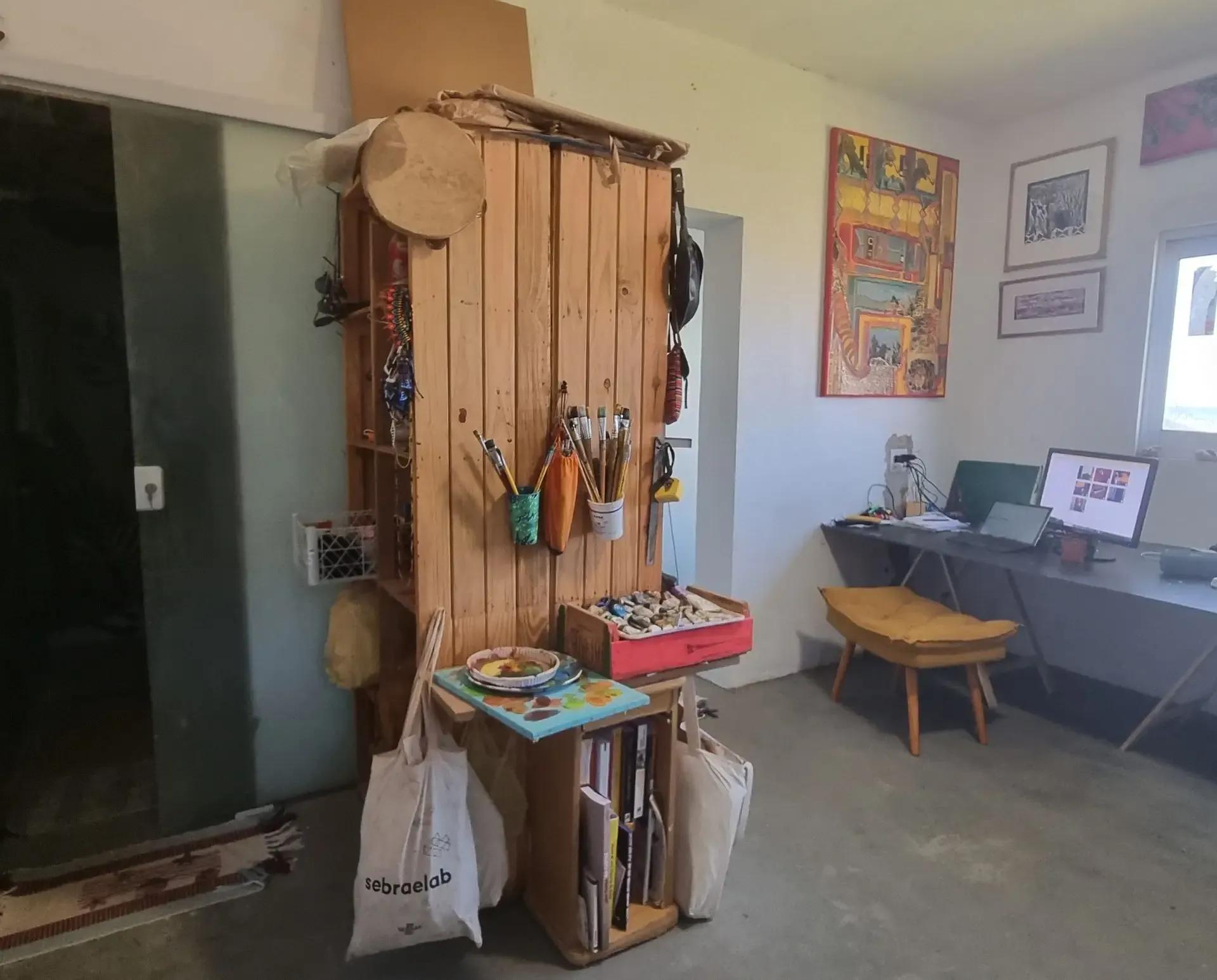 The Saraswati atelier room showing an art supply storage unit, paintings on the wall, and a desk with a computer.