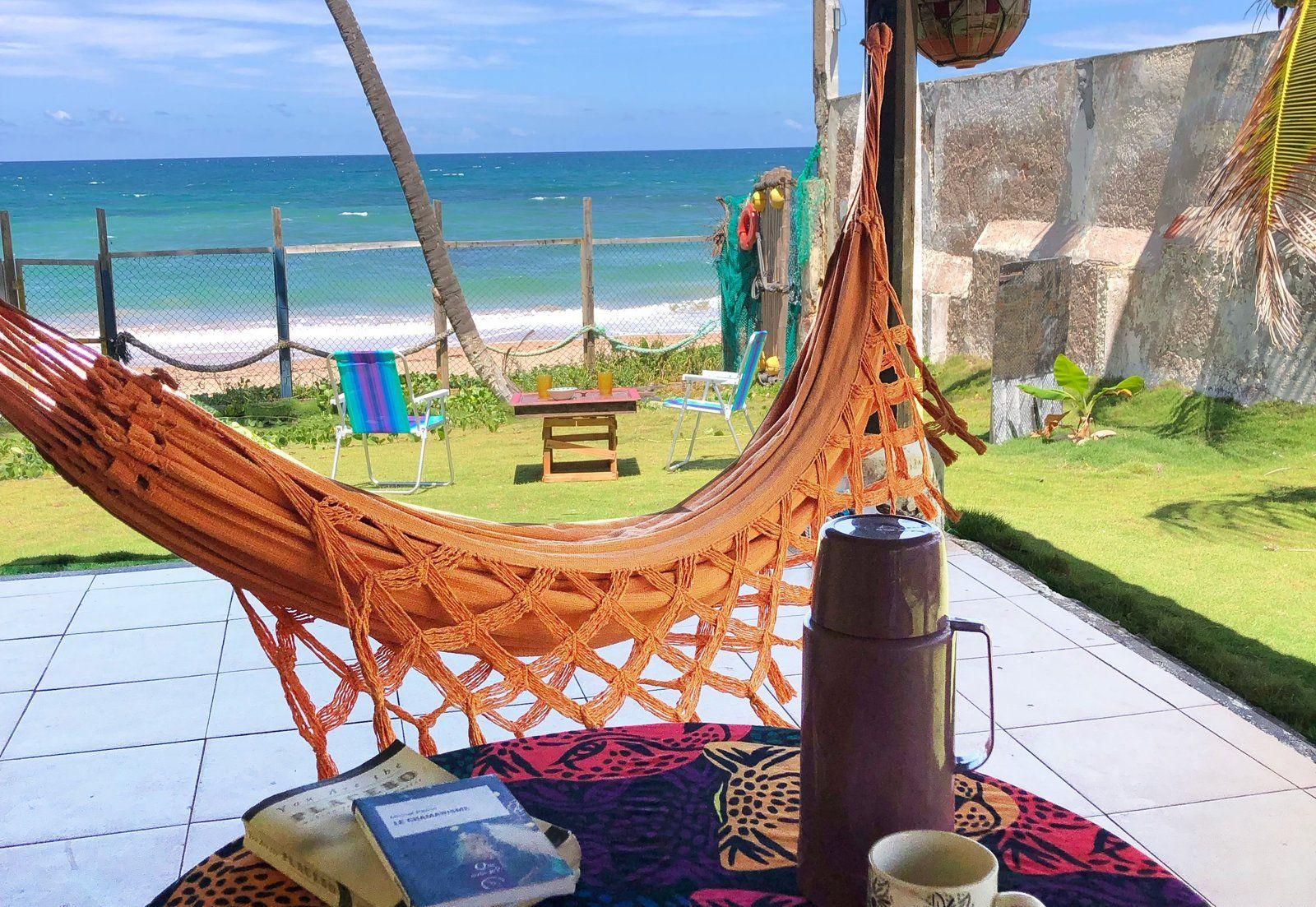 Terrace area with an orange hammock, coffee thermos, book, and a direct view of the beach and ocean.