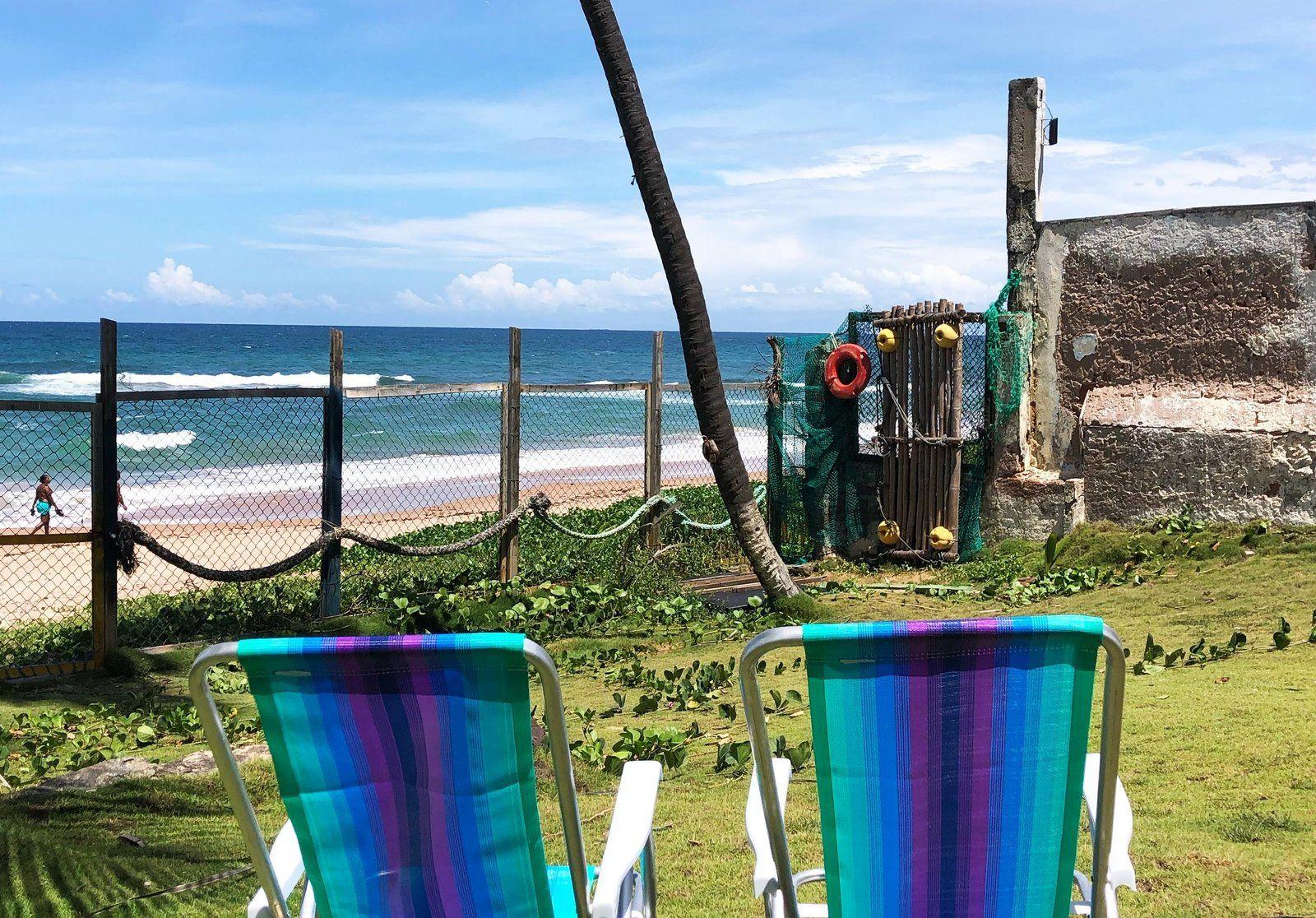 Two colorful beach chairs in the garden area with a direct view of the beach and ocean through the fence.