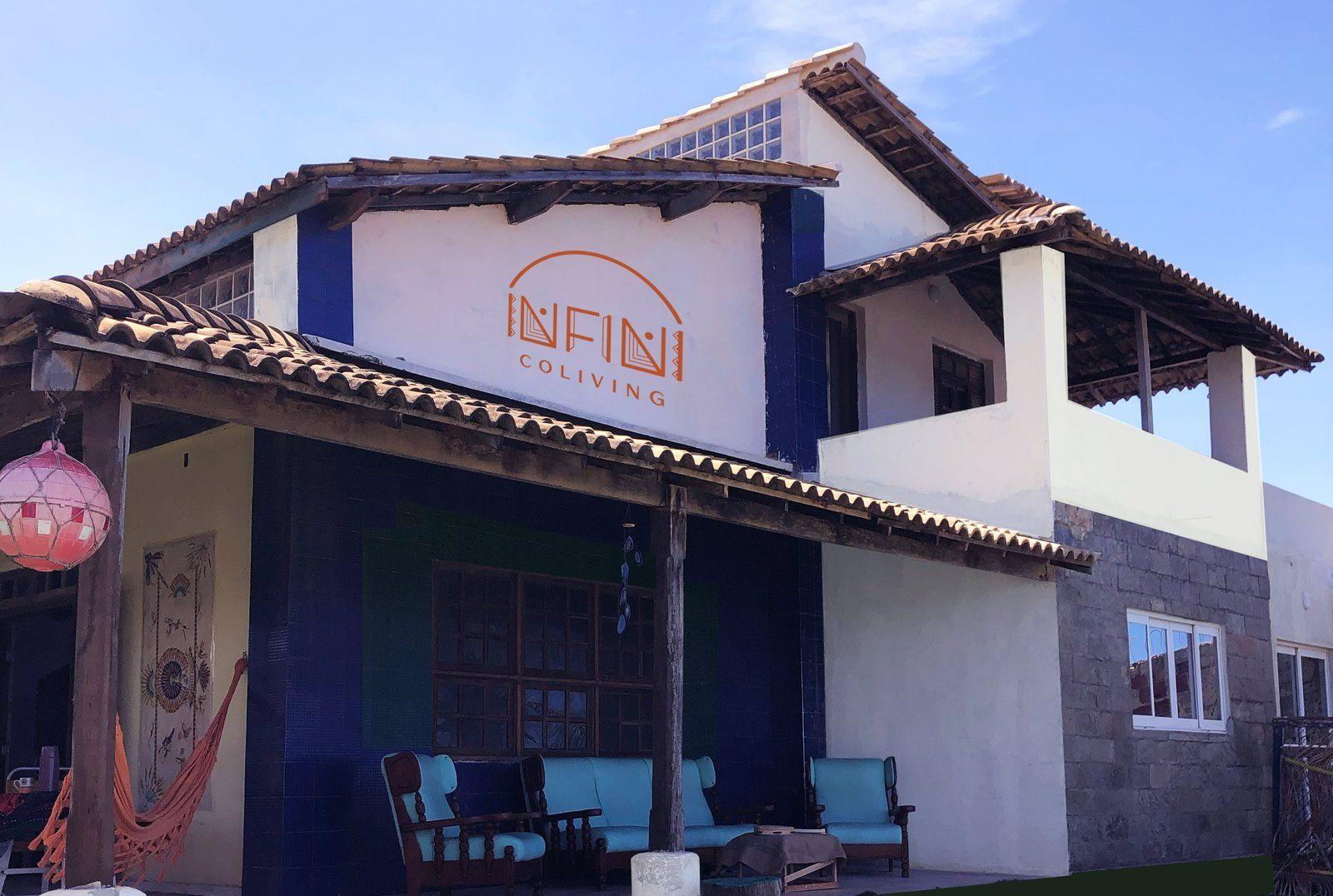 Front facade of the Infini Coliving building showing the orange logo/signage, covered terrace with hammock and seating area.