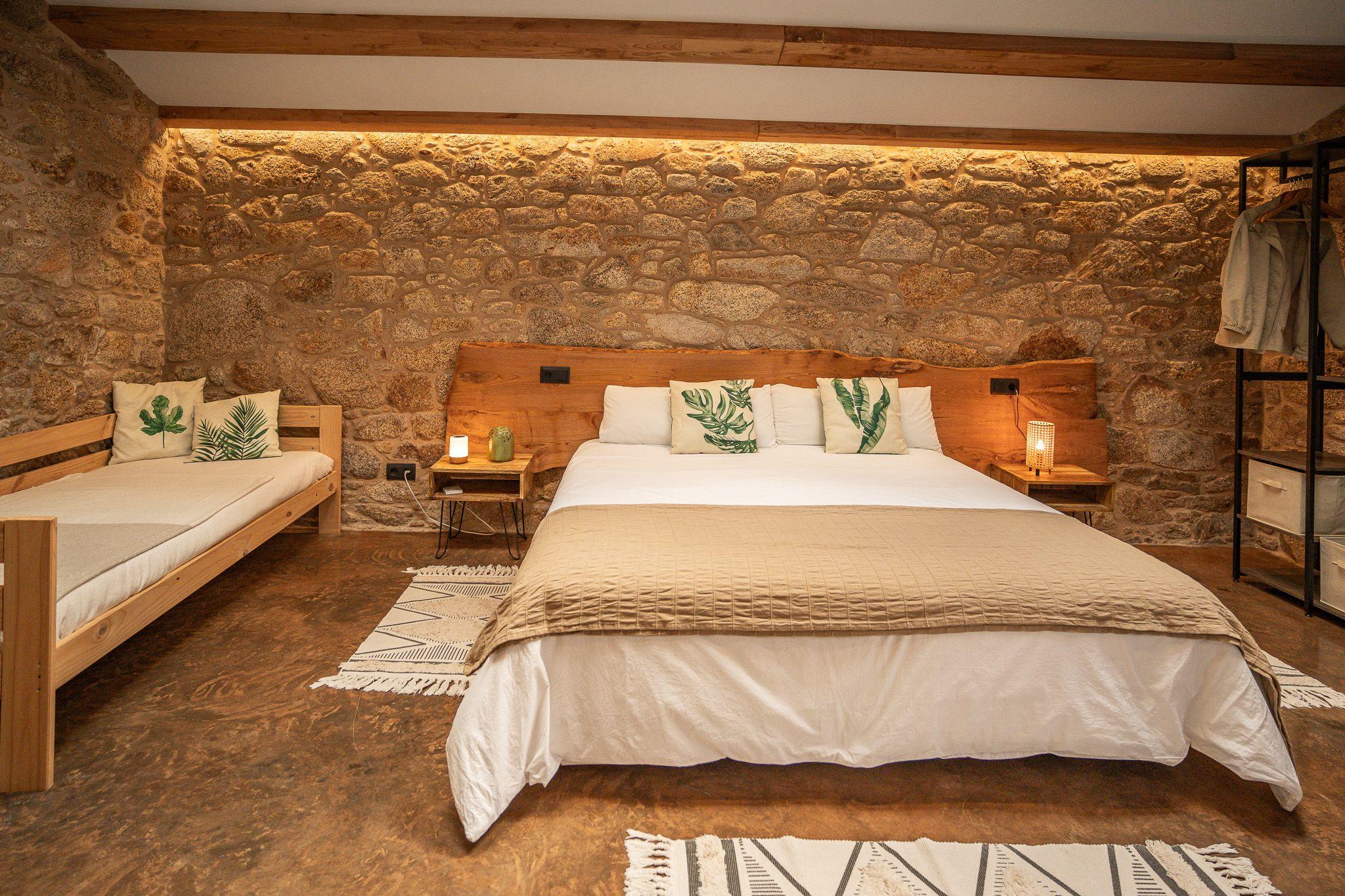 Family room O Galiñeiro with large double bed, sofa bed, stone wall with warm lighting, and wooden furnishings