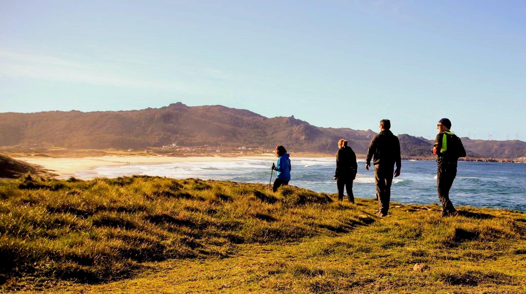 Group of hikers walking along the Galician coastline with beach and mountains in the background