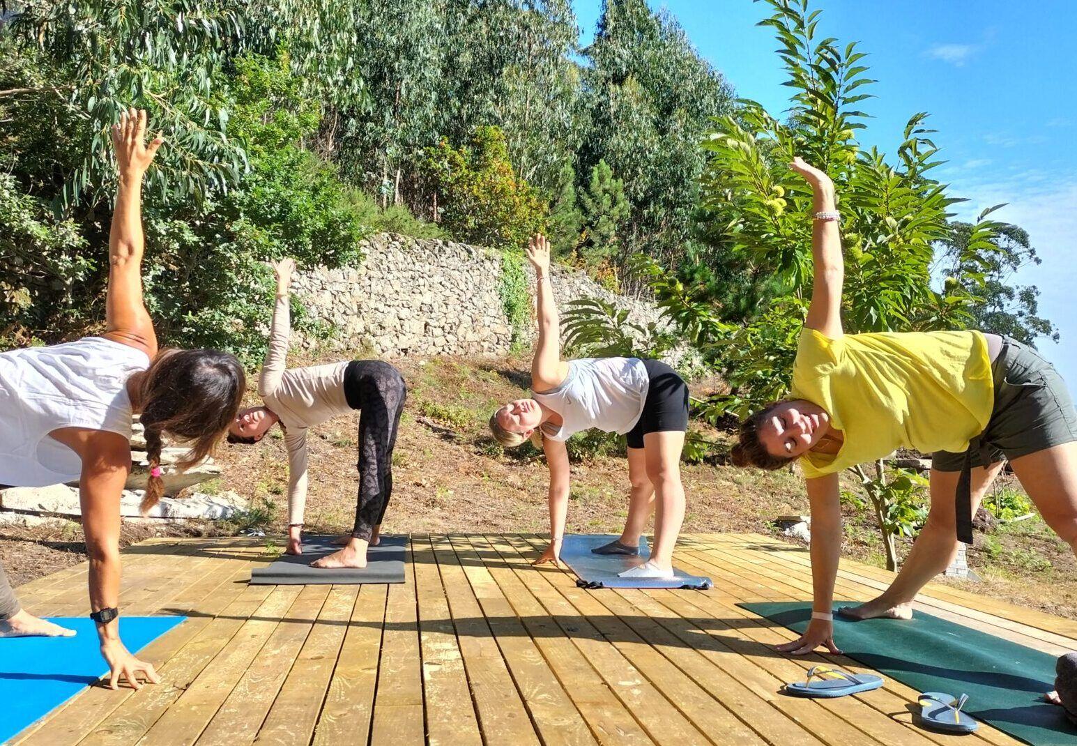 Group of four people doing yoga on the outdoor wooden yoga deck surrounded by trees and garden