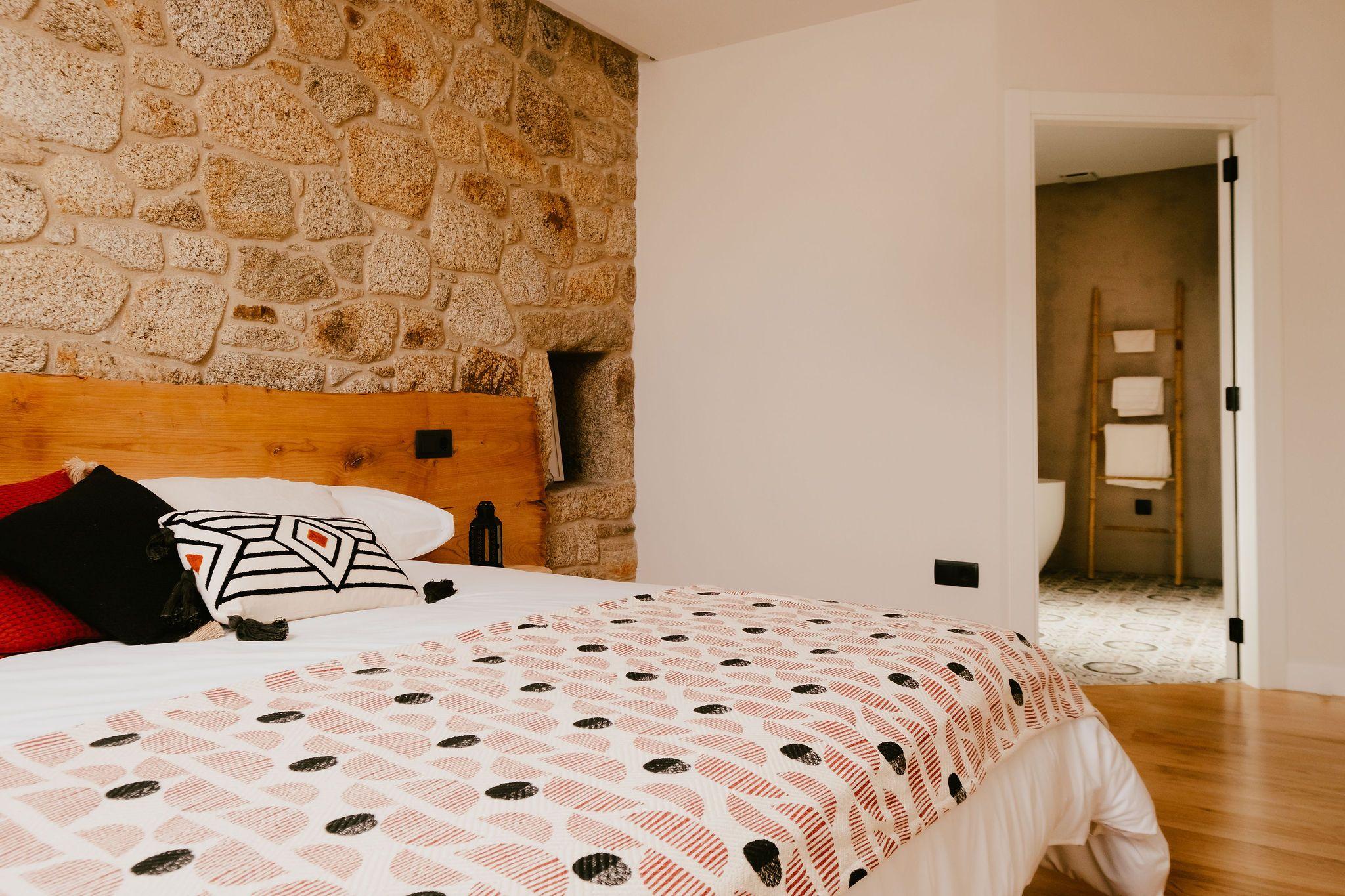 Premium double room O Avó with large double bed, stone wall, wooden headboard, and en-suite bathroom visible