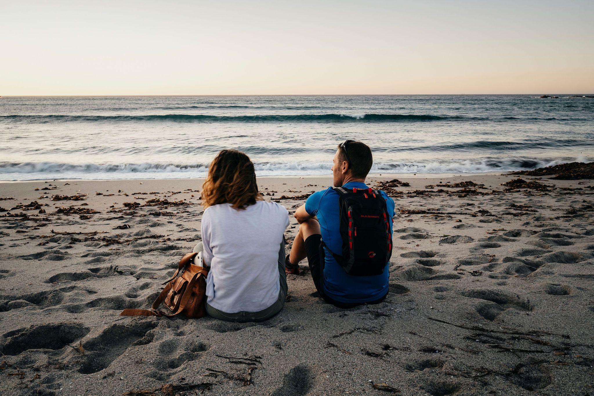 Two people sitting on the beach watching the ocean at sunset in Costa da Morte