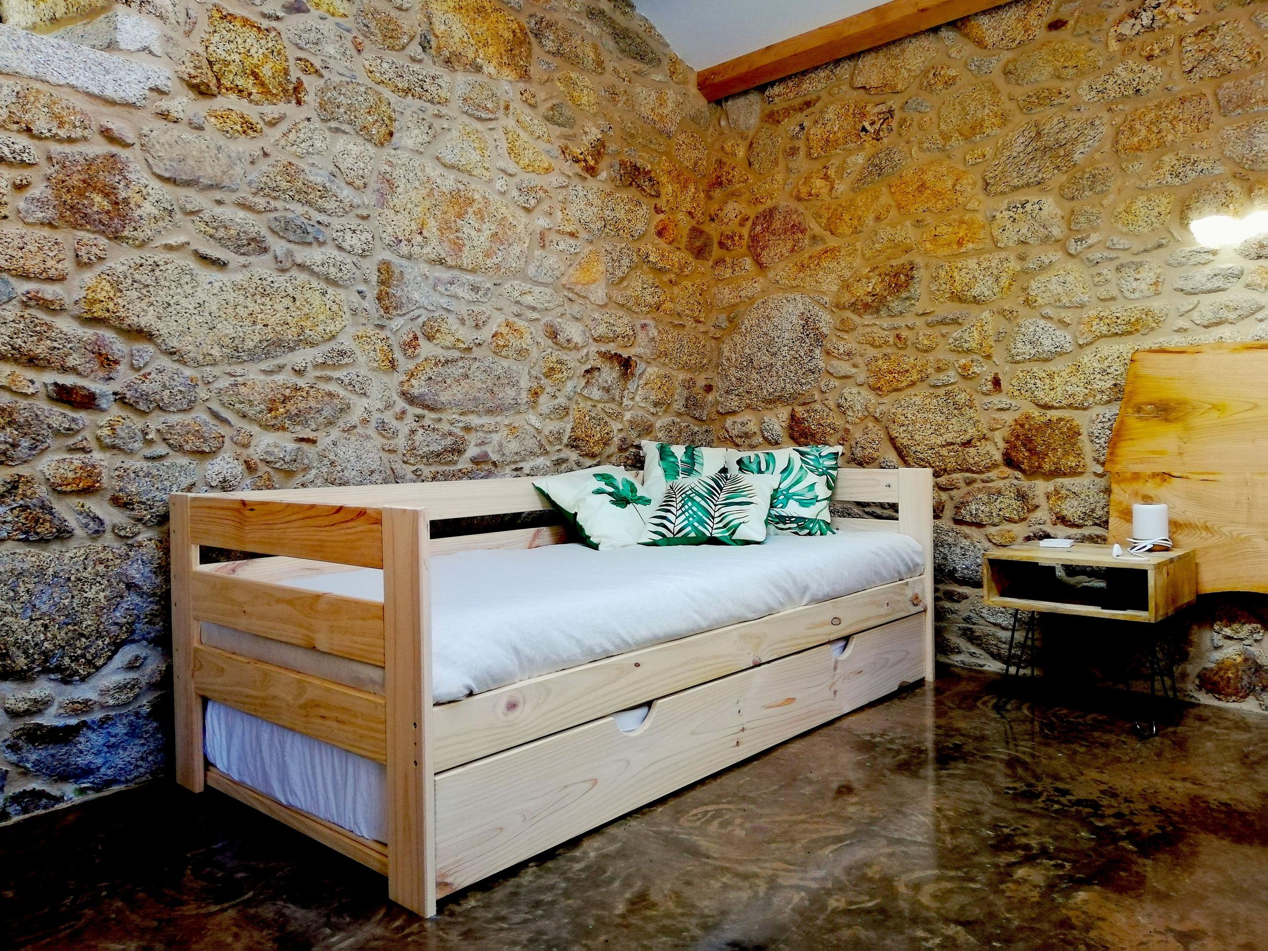 Wooden sofa bed with leaf-print cushions against a stone wall in the O Galiñeiro family room