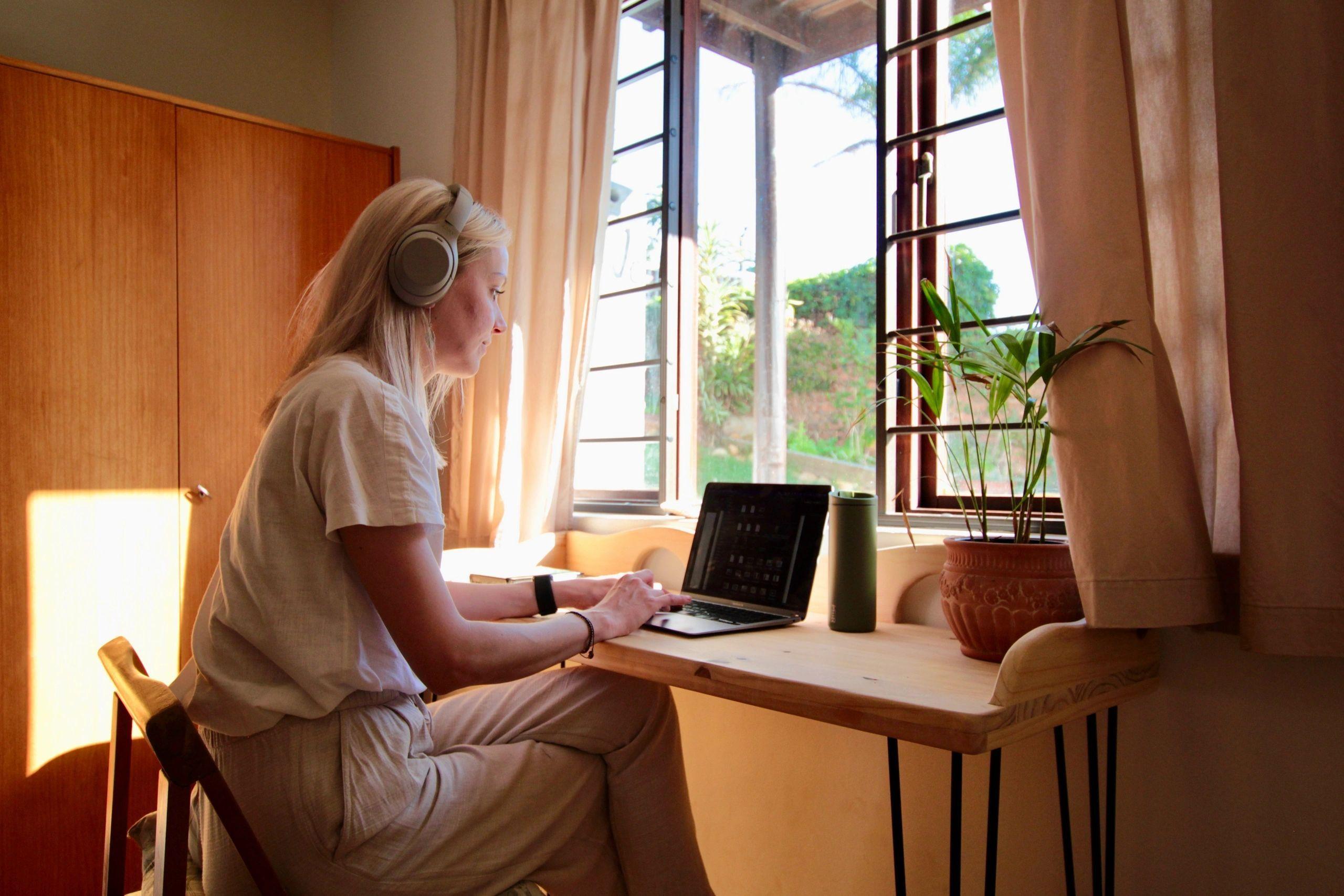 Resident with headphones working on a laptop at a desk by a sunny window in a bedroom