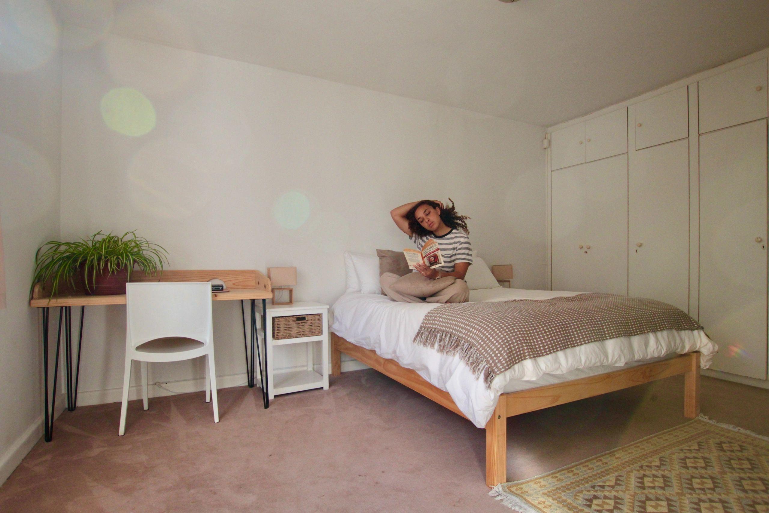 Resident sitting on a single bed reading a book in a bright room with wardrobe and desk