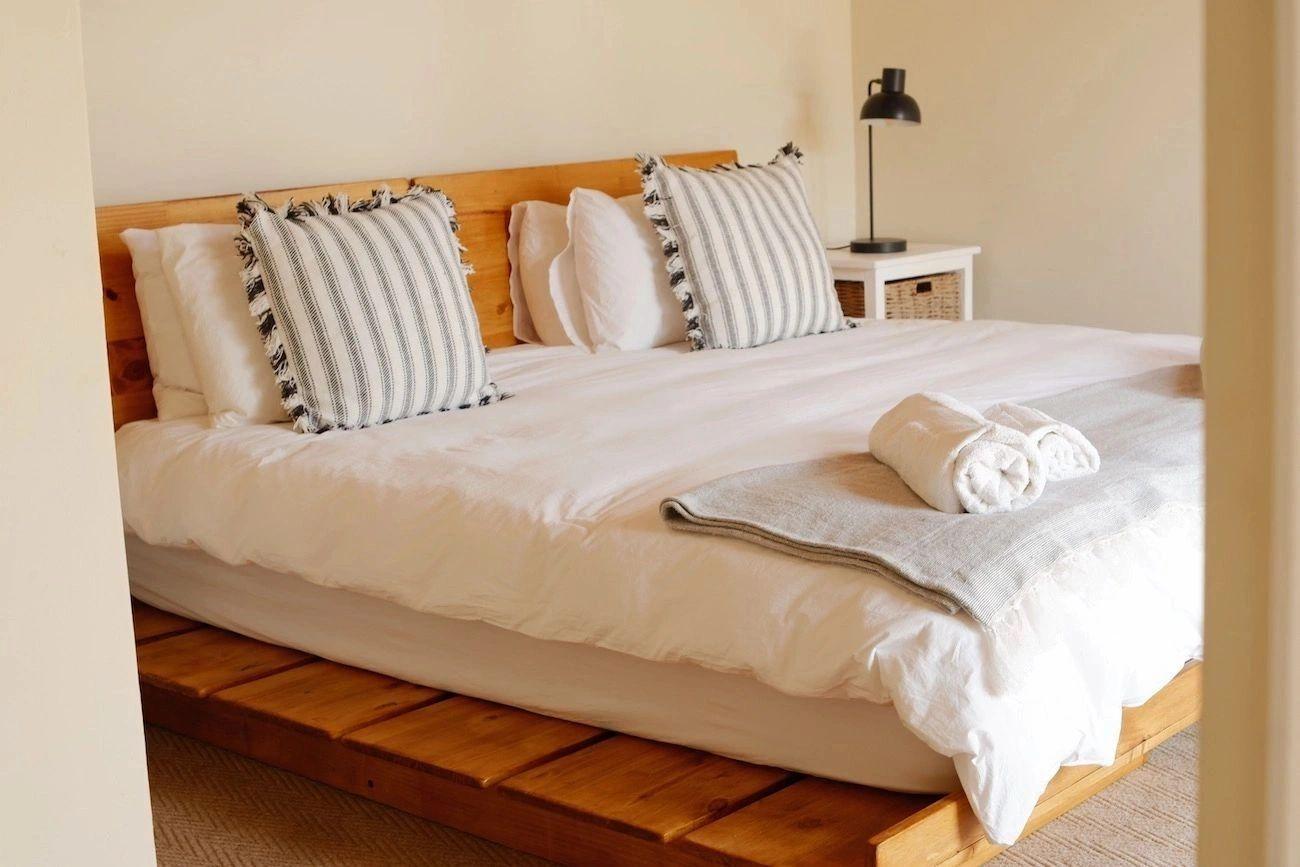 Bright bedroom with a king-size bed on a wooden platform frame, striped pillows, and luxury linen