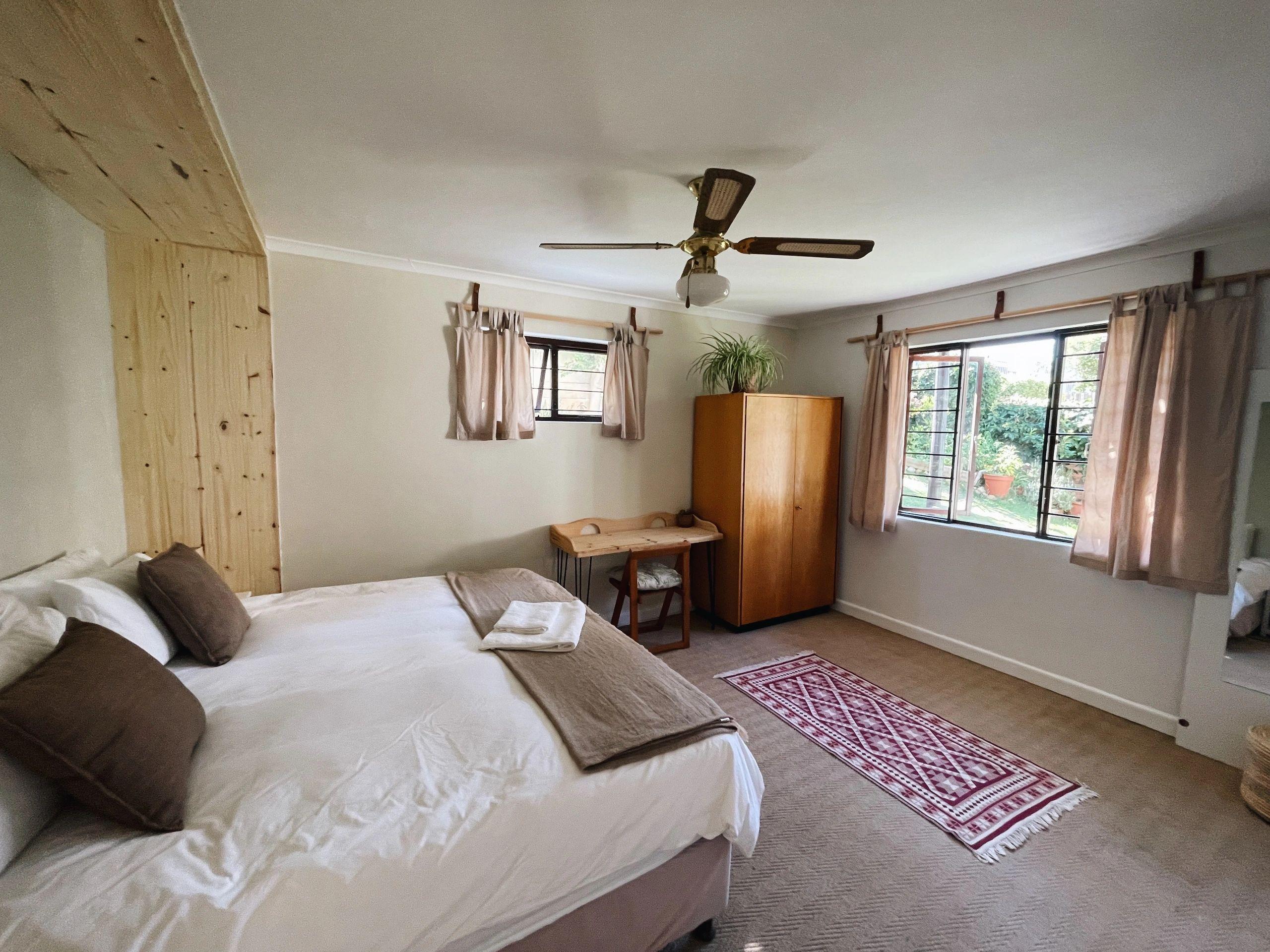 Ground floor bedroom with a double bed, ceiling fan, wardrobe, desk, and garden-facing windows