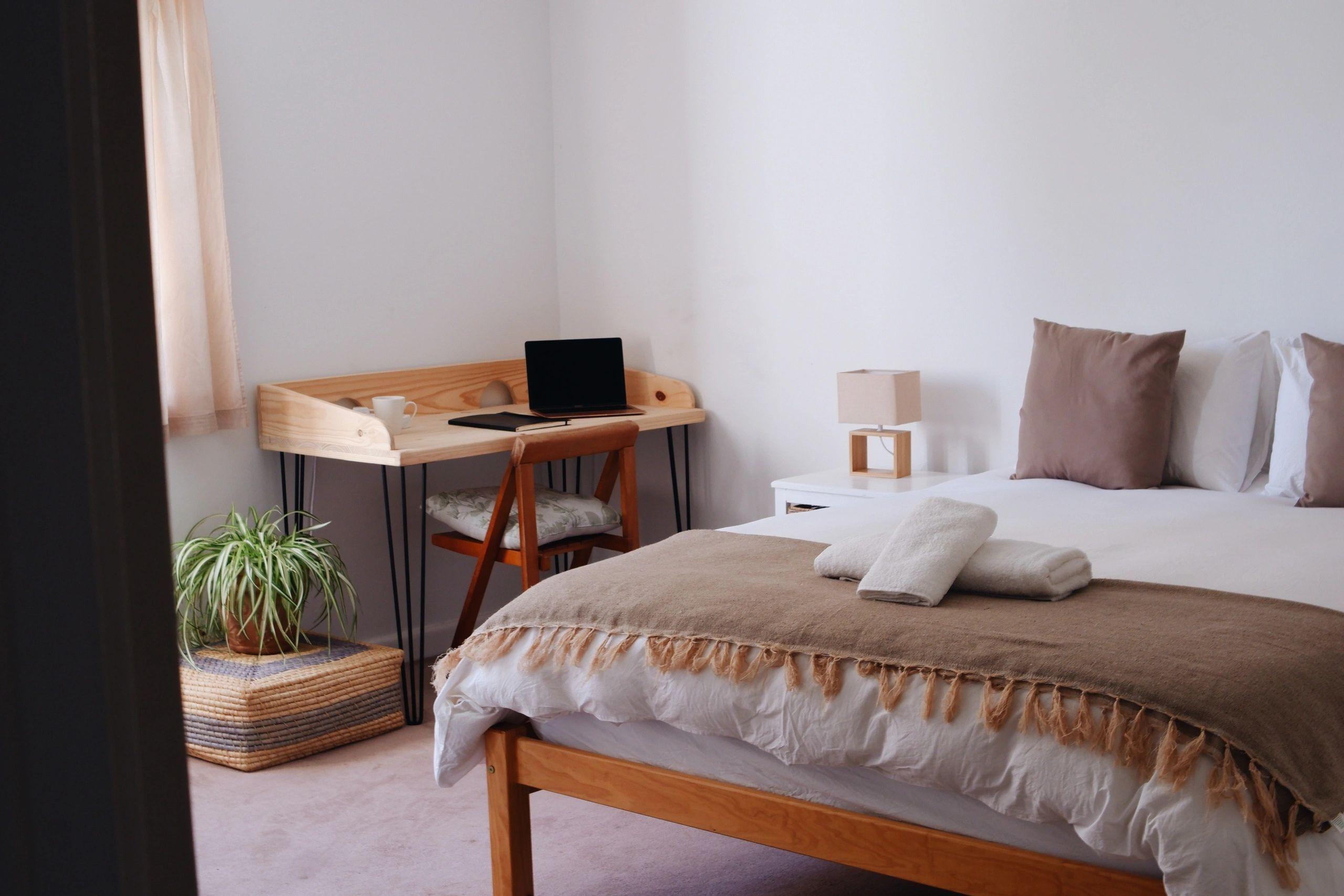Bedroom with a double bed, wooden desk with laptop, bedside lamp, and plant