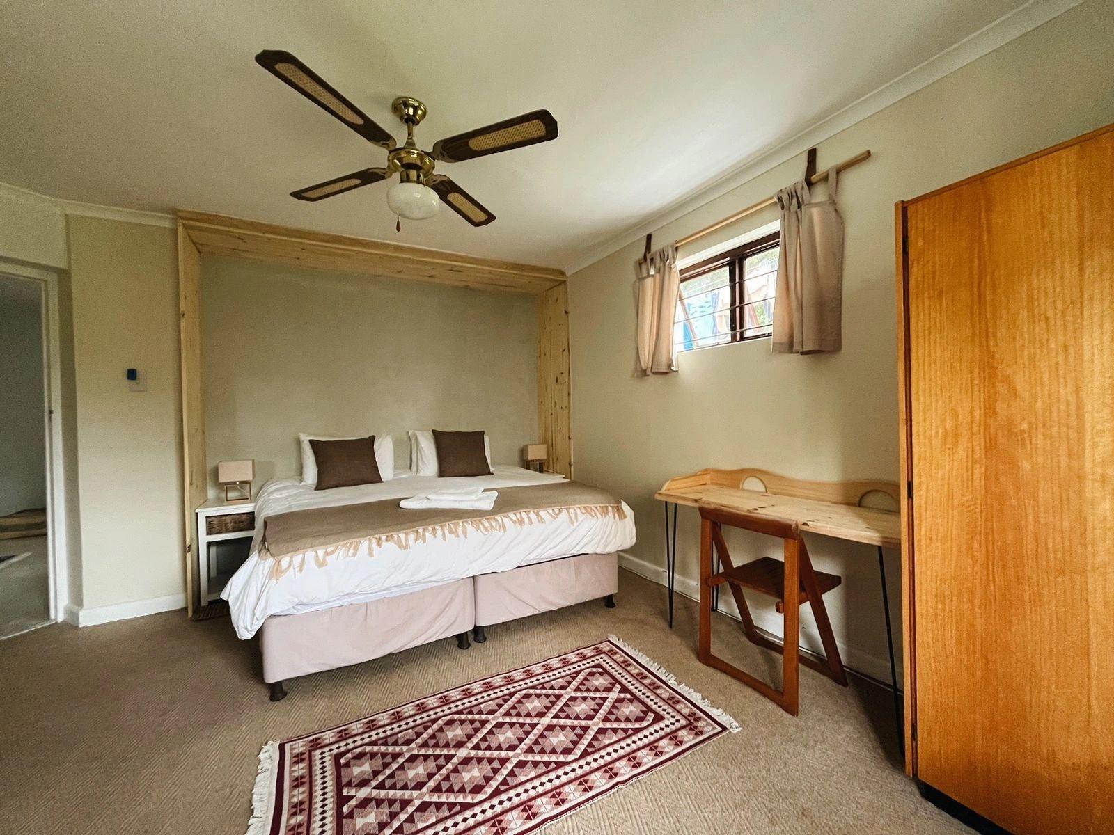 Ground floor bedroom with a double bed, ceiling fan, wooden wardrobe, desk, and garden-facing windows
