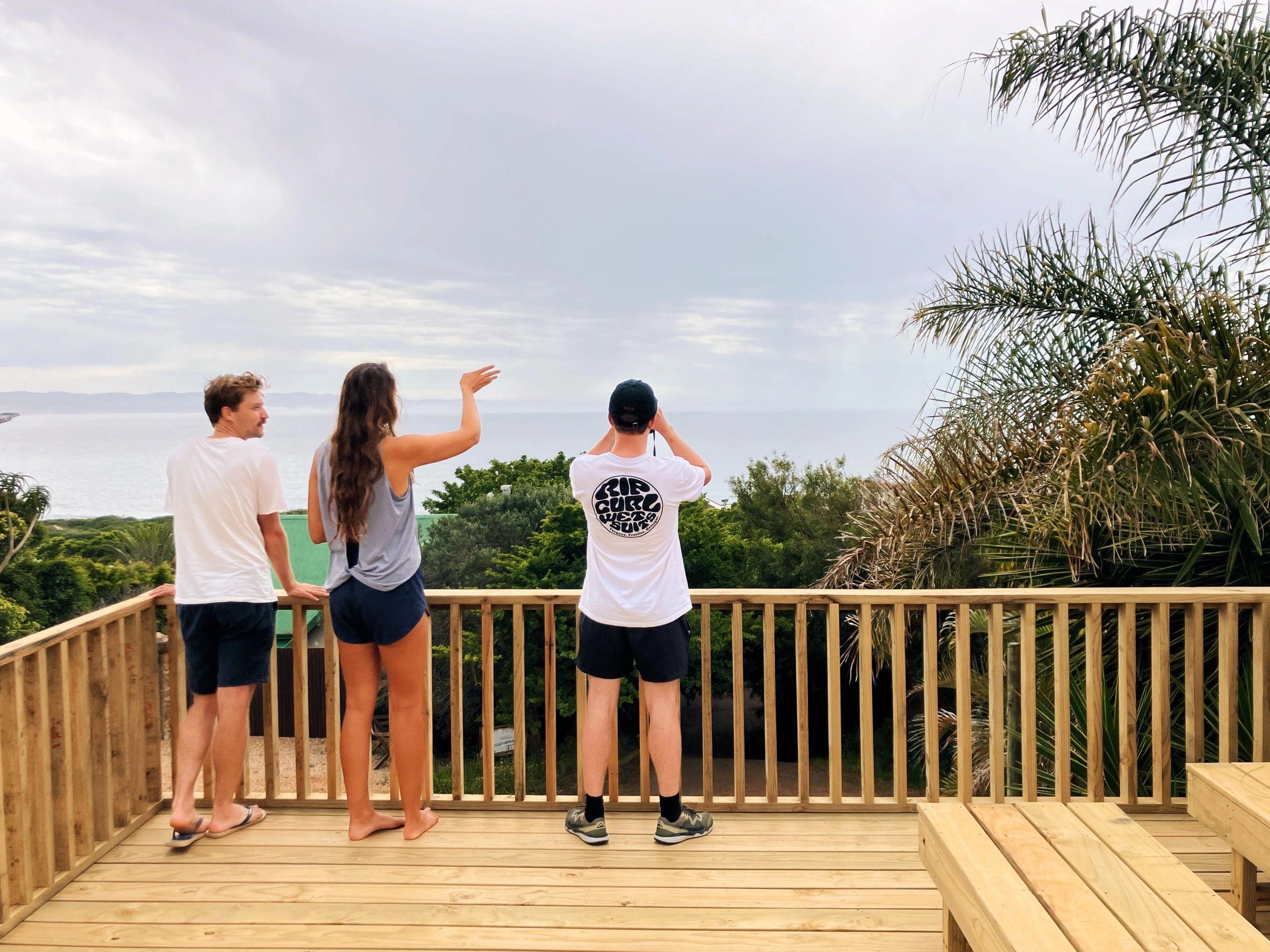 Three residents standing on the wooden sundeck looking out over the ocean and surrounding landscape