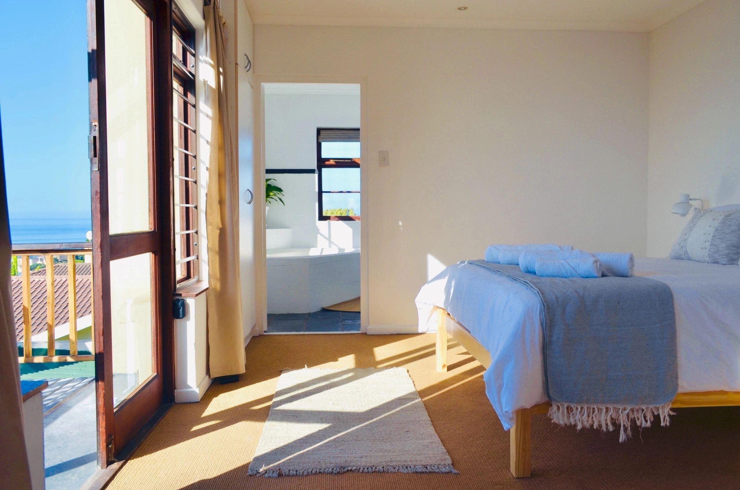 Bright bedroom with a double bed, ocean view through large windows and balcony doors, and en-suite bathroom visible
