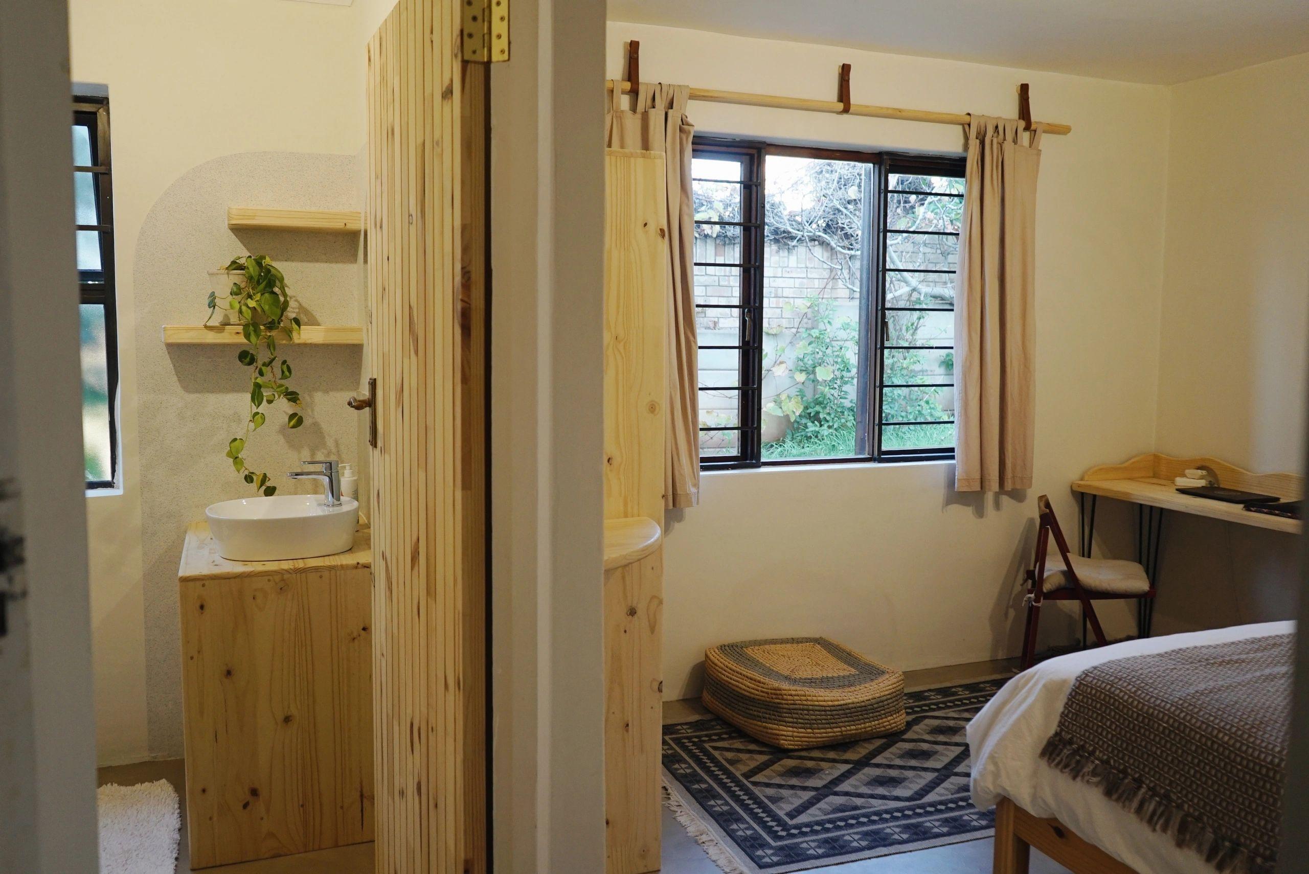 En-suite bathroom with wooden vanity, round mirror, shelves with plants, and tiled walls