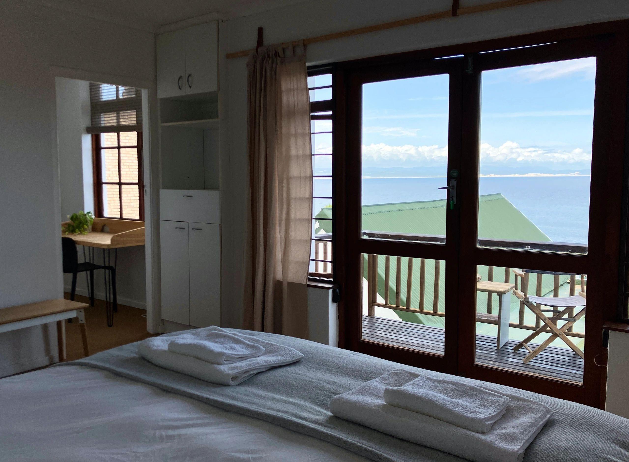 Bedroom with a double bed, wardrobe, desk, and large windows with ocean view and private terrace