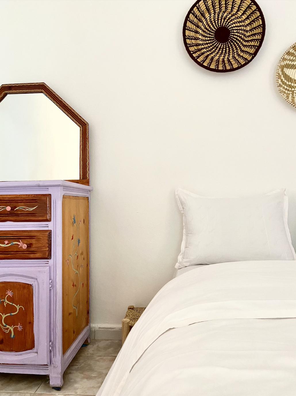 Private room with a single bed, painted dresser with mirror, and woven wall decorations