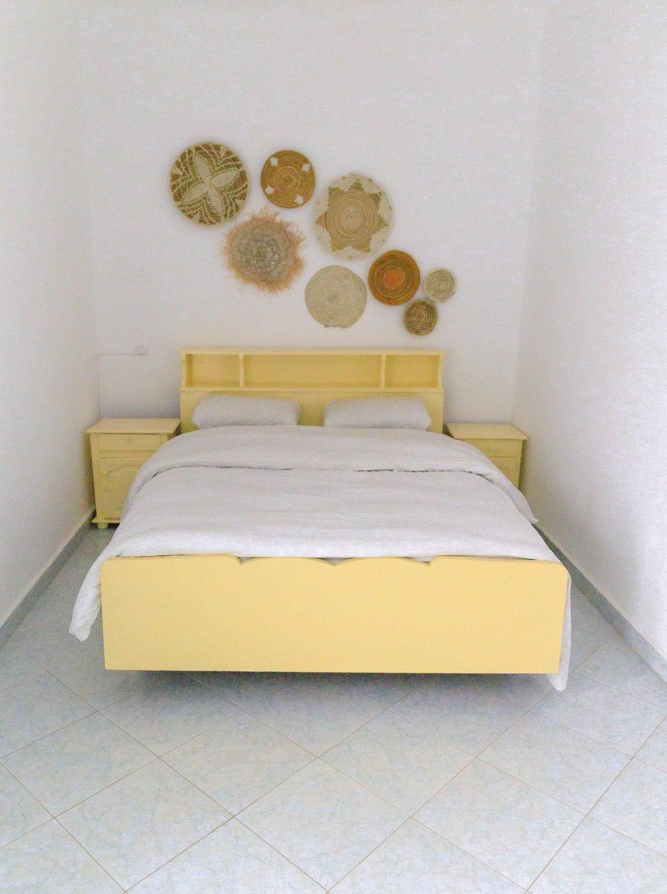 Private room with a double bed with yellow frame and woven basket wall decorations